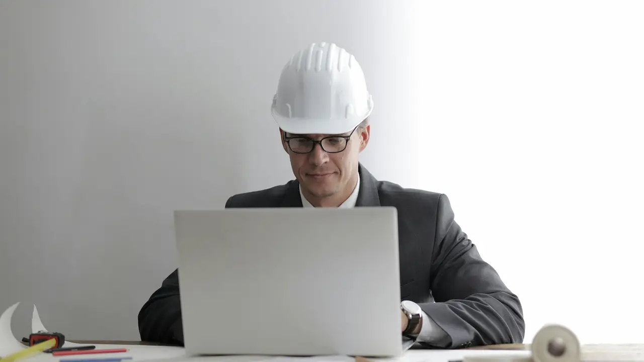 Serious architect working on laptop with blueprints as a freelancer.