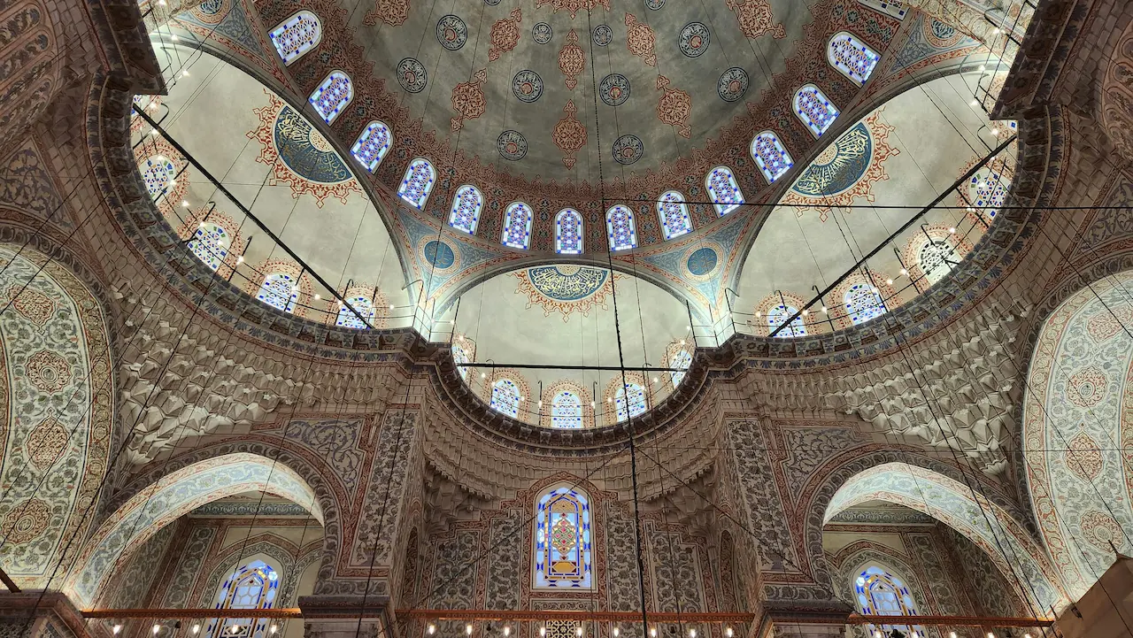 Interior view of the Blue Mosque in Istanbul, Türkiye, highlighting its intricate tilework and grand chandeliers.
