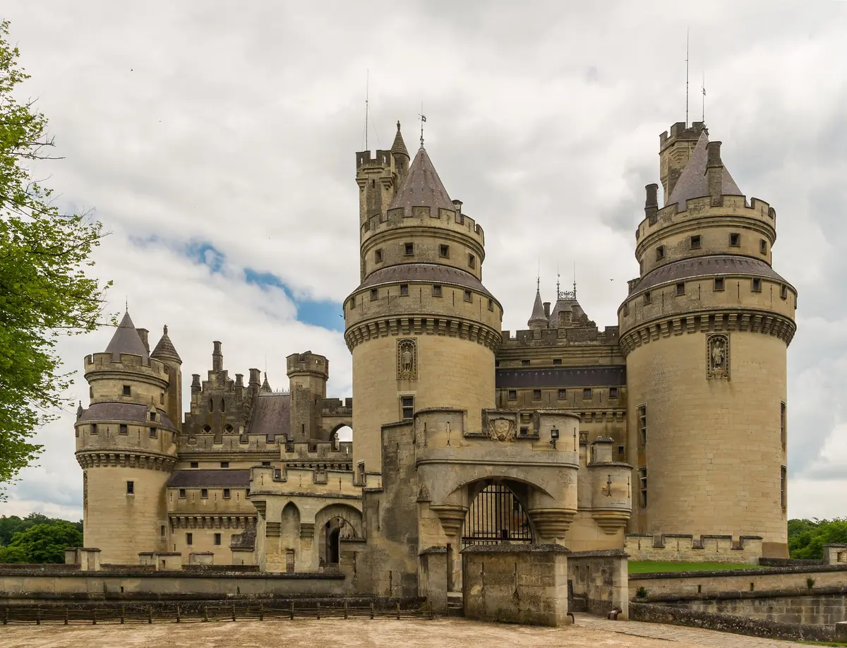 Château de Pierrefonds, a medieval castle with imposing towers, crenelated walls, and a picturesque setting surrounded by lush greenery.