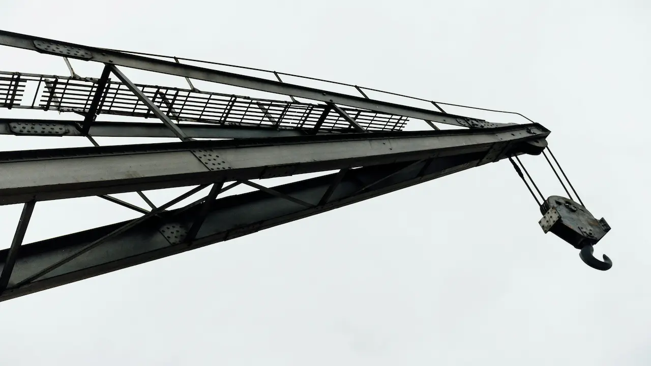 Crane arm with hook towering over a construction site under development.