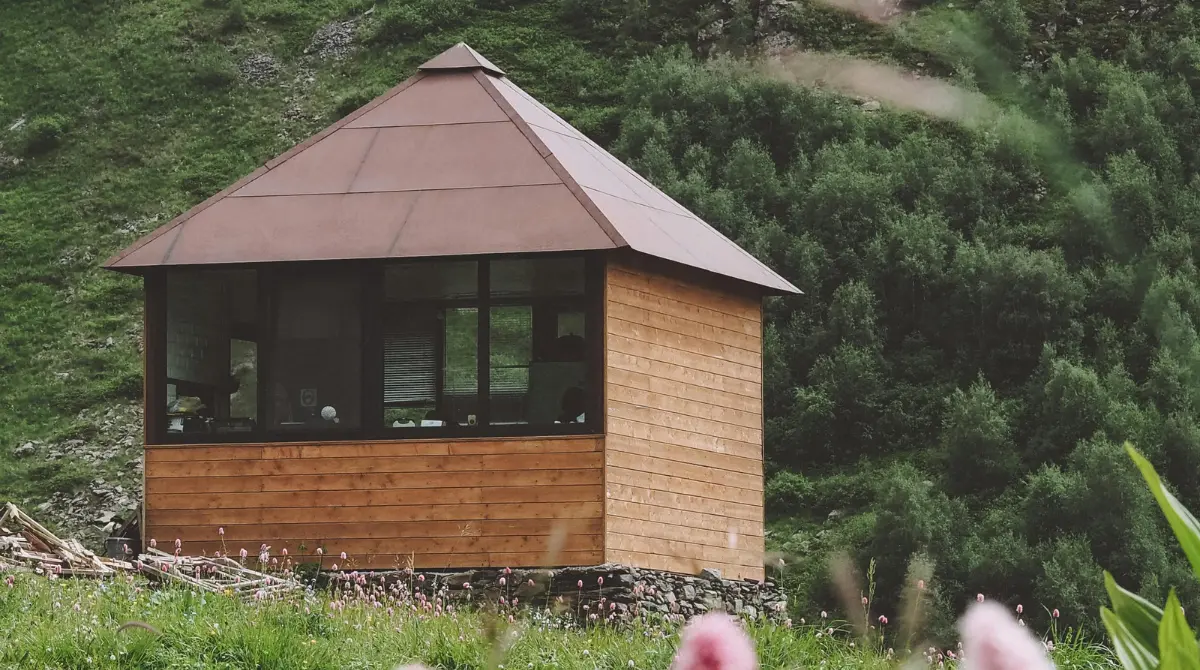 A contemporary small house with modern design, situated behind blooming flowers in a meadow.