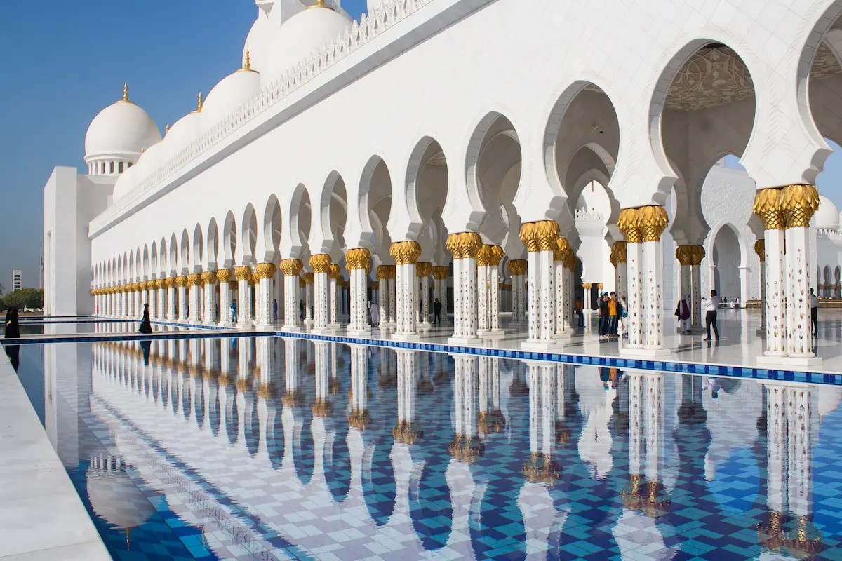 The Grand Mosque in Abu Dhabi featuring white marble domes, intricate Islamic calligraphy, and reflective pools under a vibrant sky.