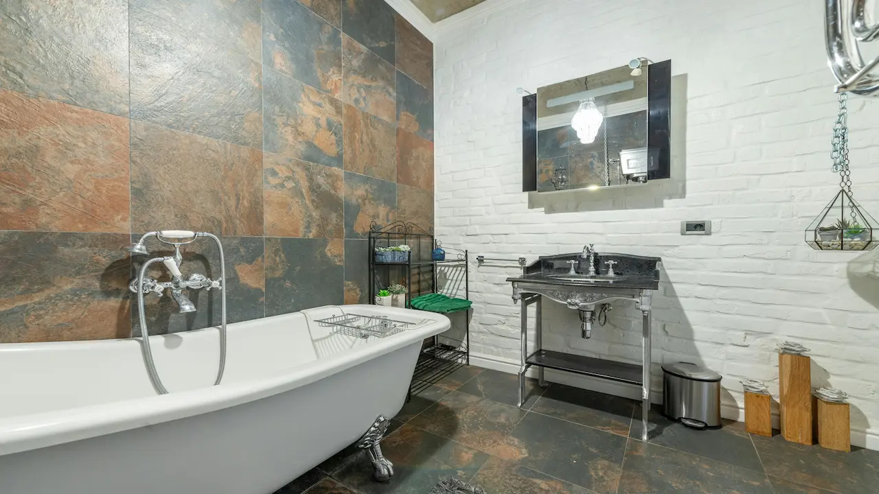 Industrial bathroom with white ceramic bathtub and stainless steel washbasin inside a shower room.