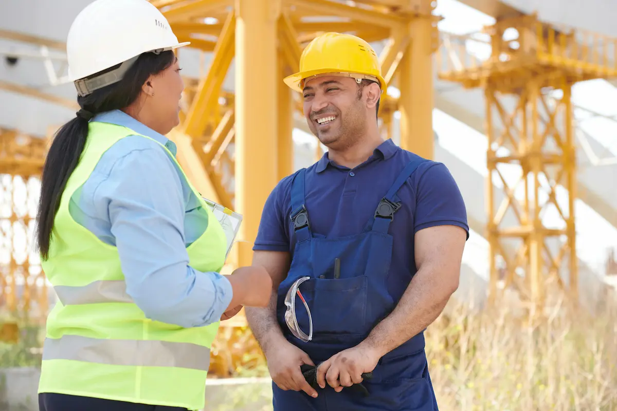 man wearing a yellow hardhat smiling at a woman in PPE