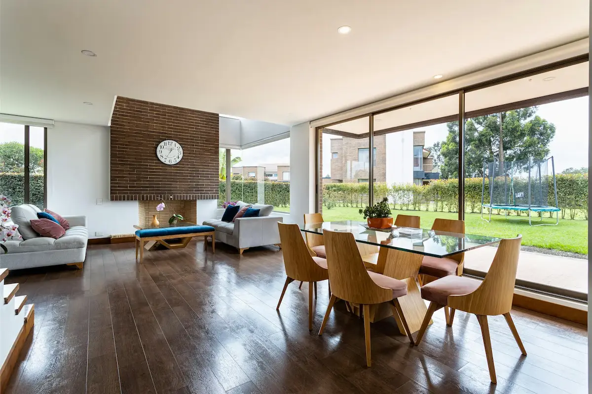 A brown wooden table and chairs beside large glass windows in a minimalist living room.
