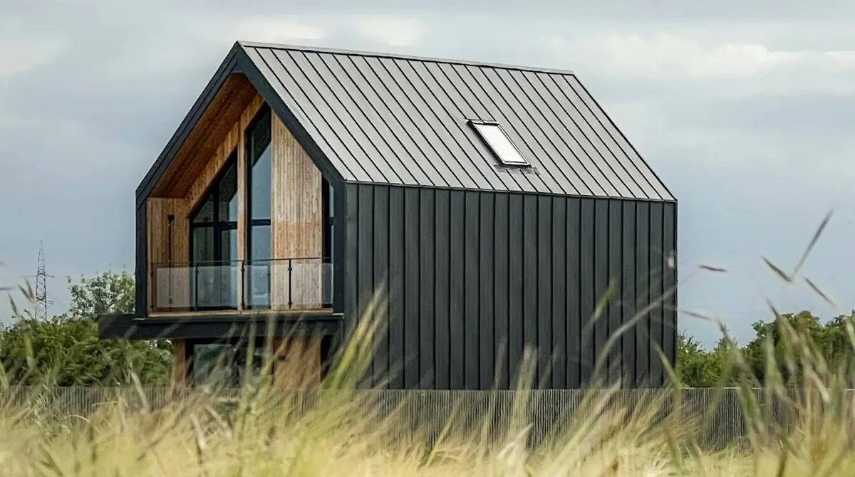A small modern house with a smart use of materials and dark exterior blends into a scenic field.
