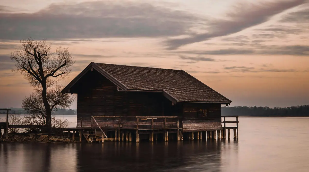 wooden pilings supporting a rustic cabin surrounded by trees and water