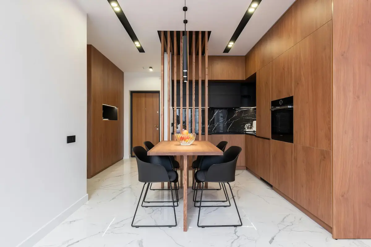 A stylish kitchen with wooden furniture, dining zone, and minimalist storage solutions, featuring floating shelves and wall-mounted units for a sleek look.