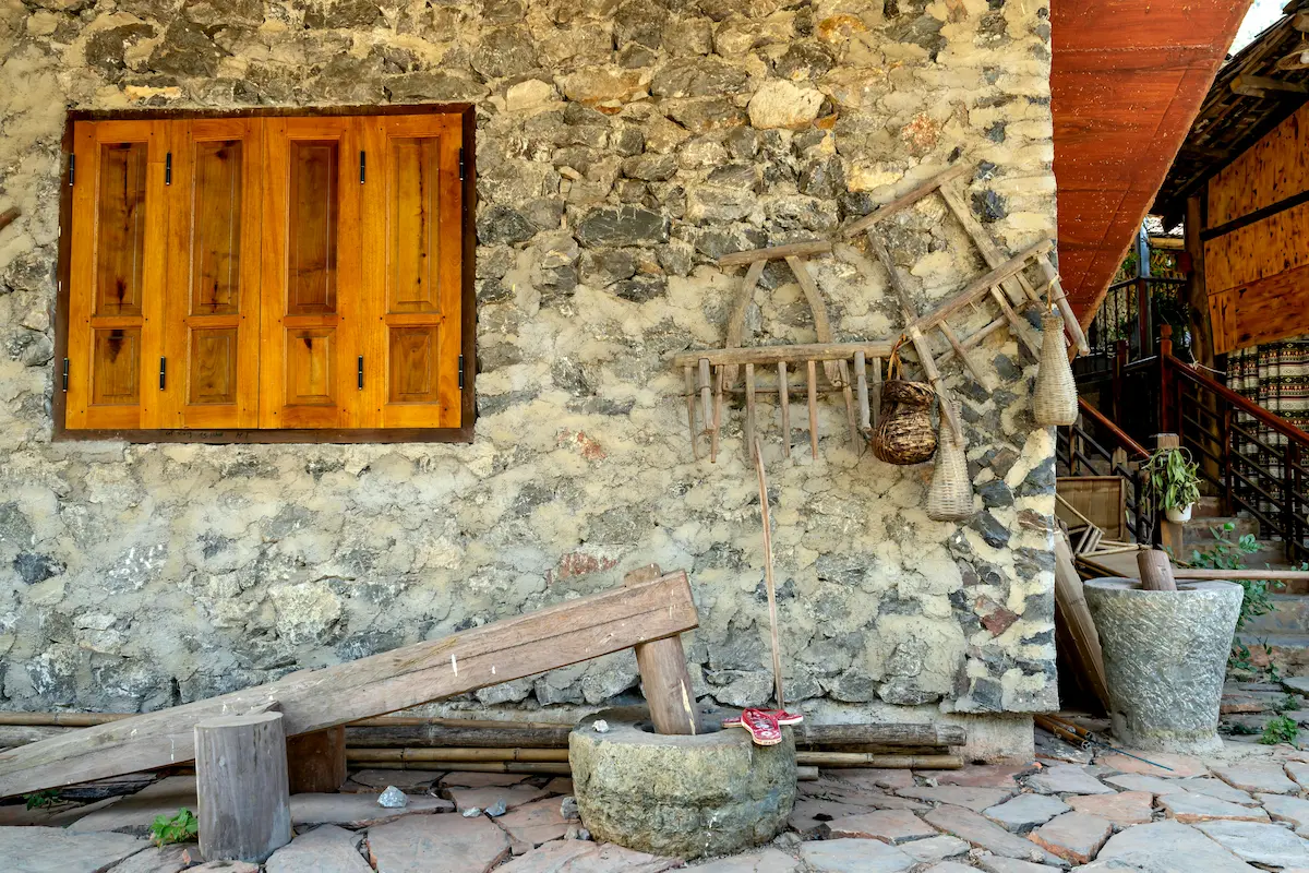 Antique wooden items outside a farmhouse constructed with vernacular materials.