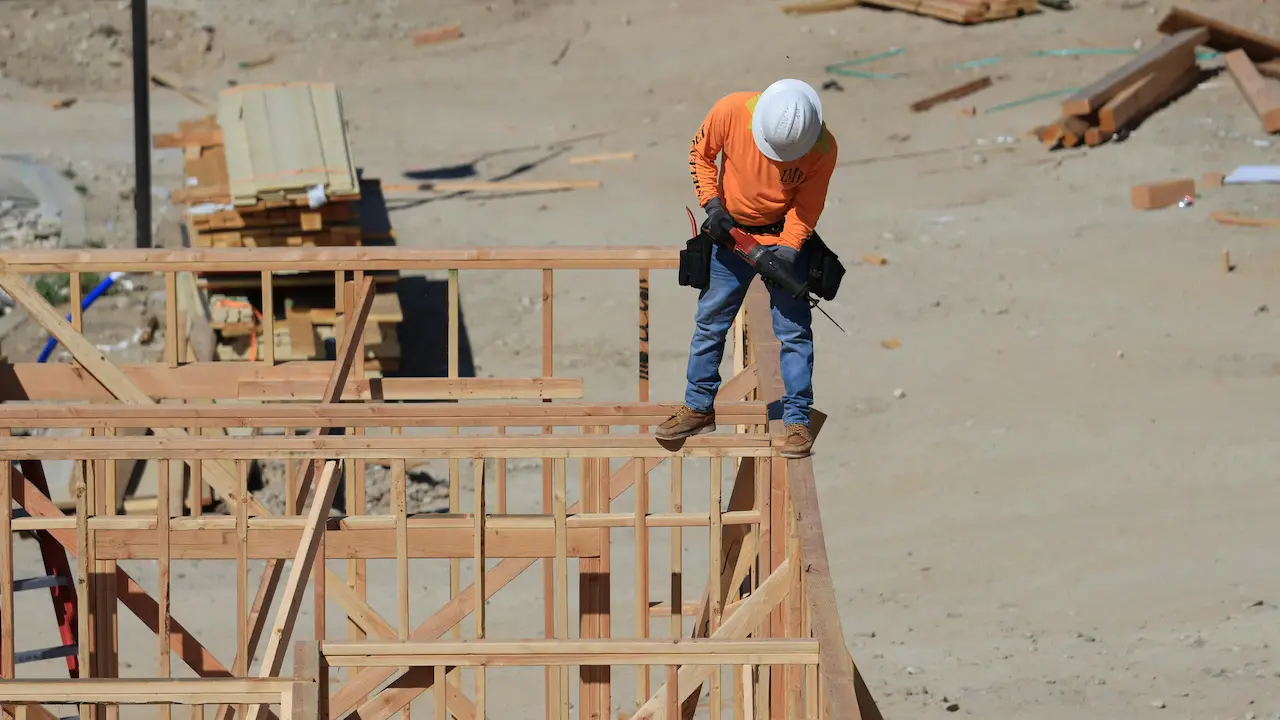 Construction worker installing truss braces on house frames at a building site.