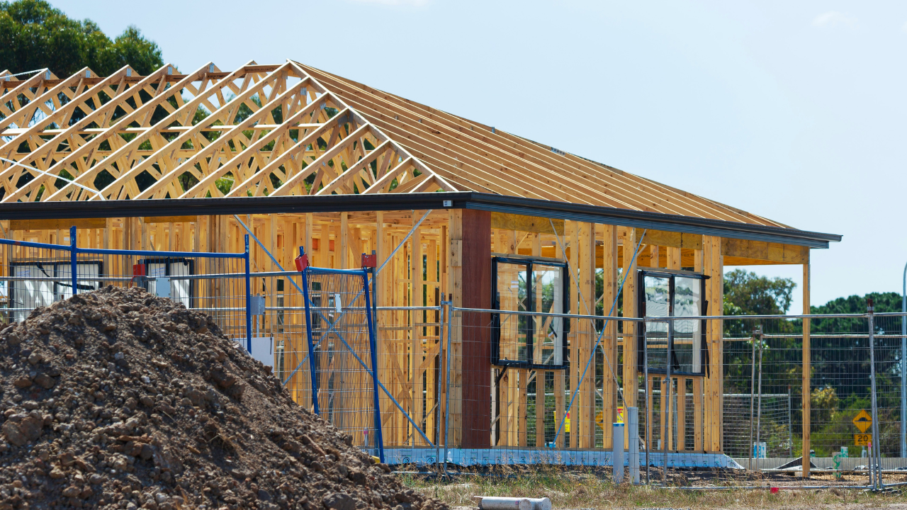 A one-story house in the framing stage, with wooden beams and structural elements visible before finishing.