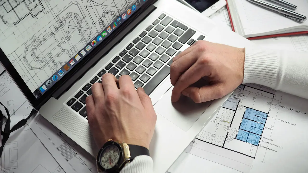 An architect reviewing blueprints and design layouts on a laptop, deeply focused on planning and problem-solving.