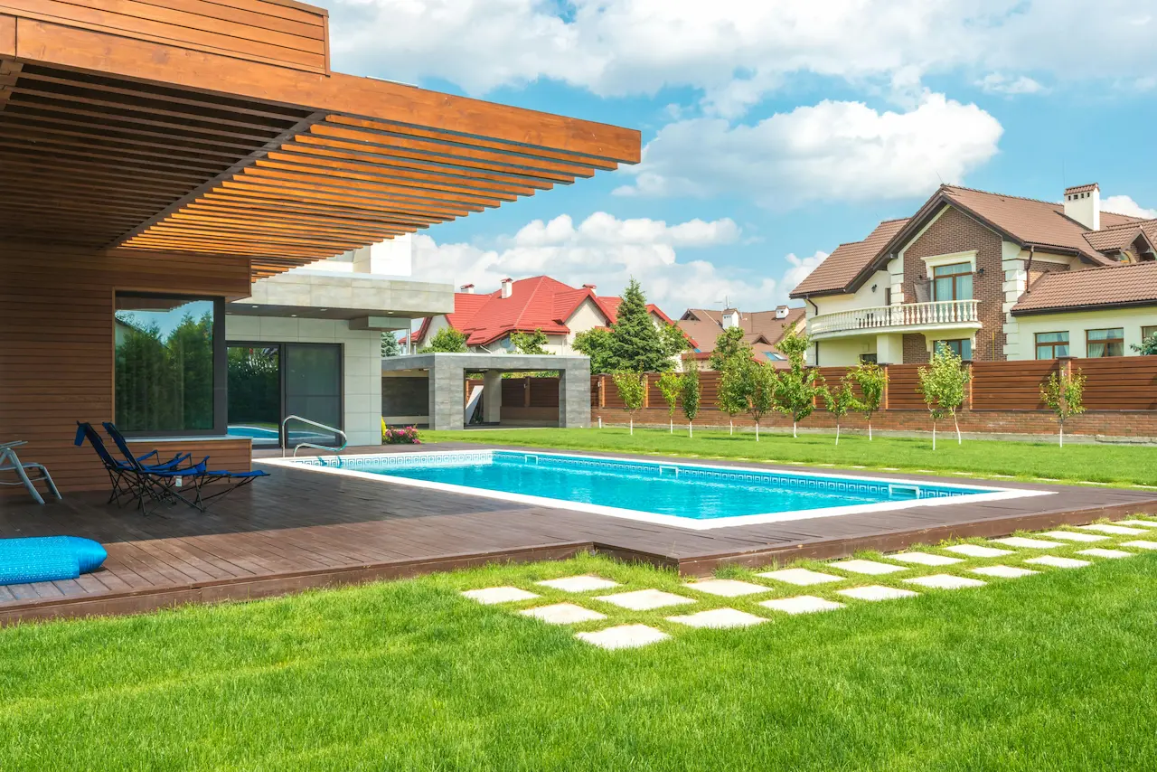 A custom home with a large patio and swimming pool, located in a serene neighborhood with greenery and a clean, modern backyard design.