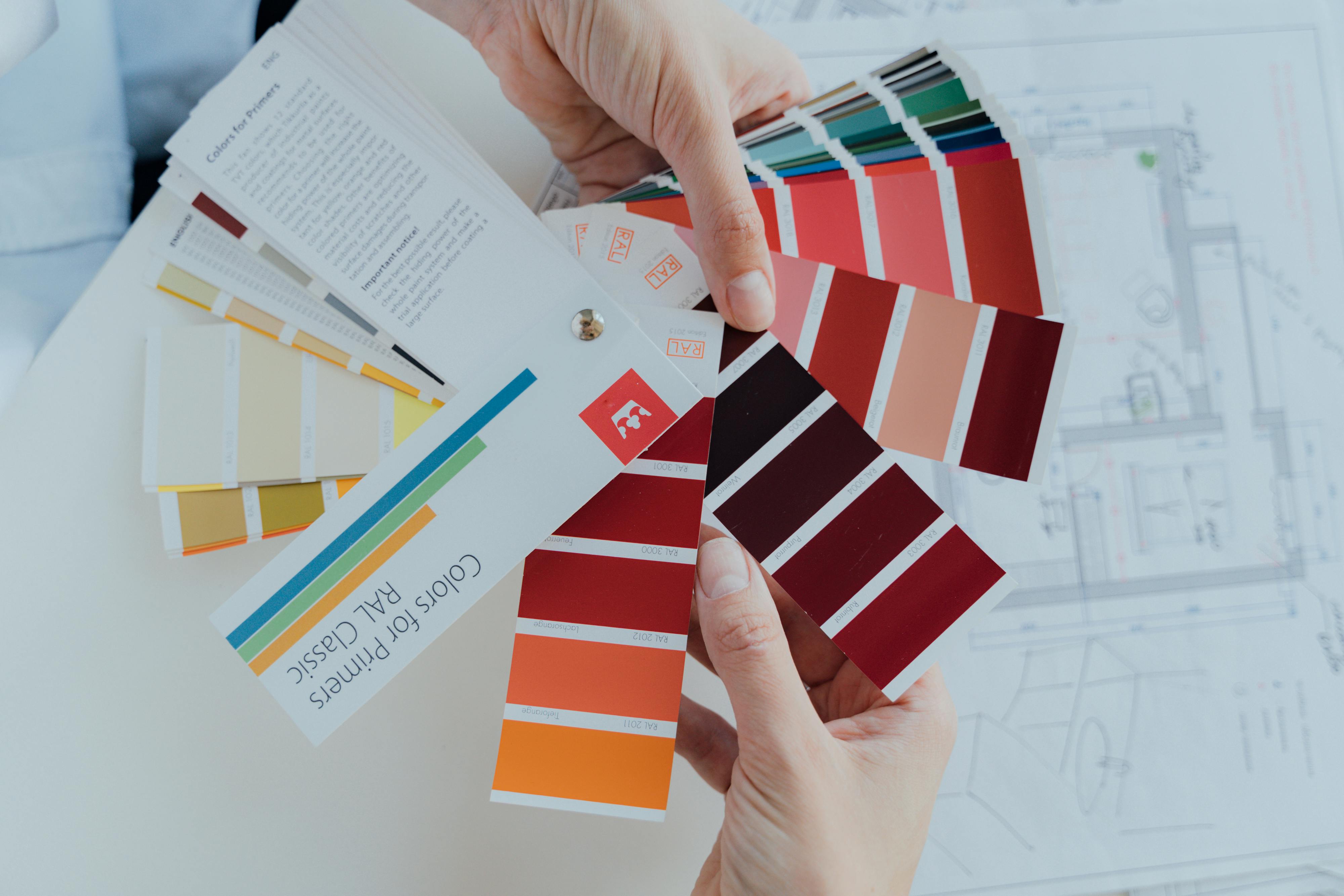 Person holding color palettes next to architectural blueprint, selecting colors for design.