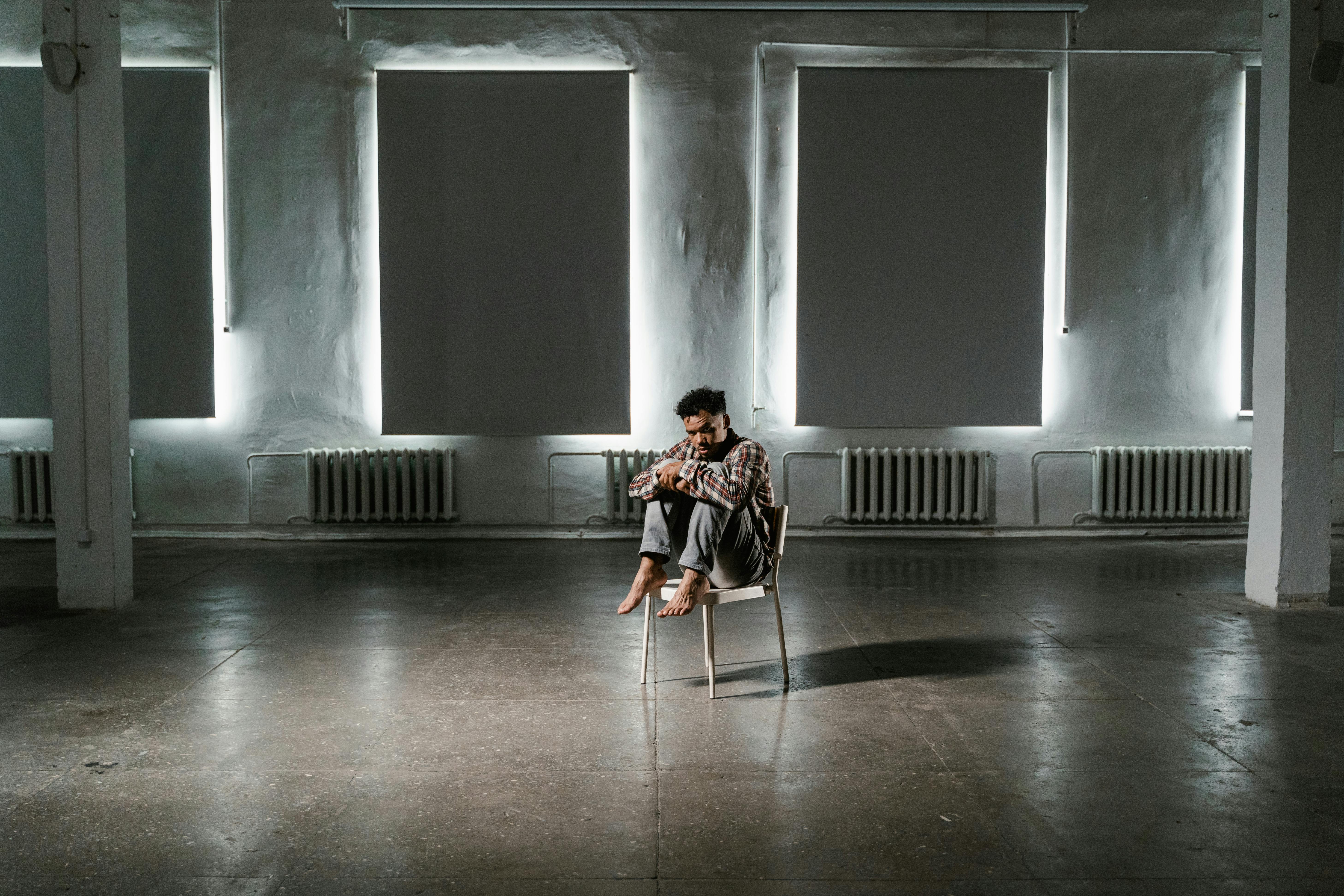 Man sitting alone in a dark, poorly designed interior with no natural light or airflow, reflecting emotional distress.