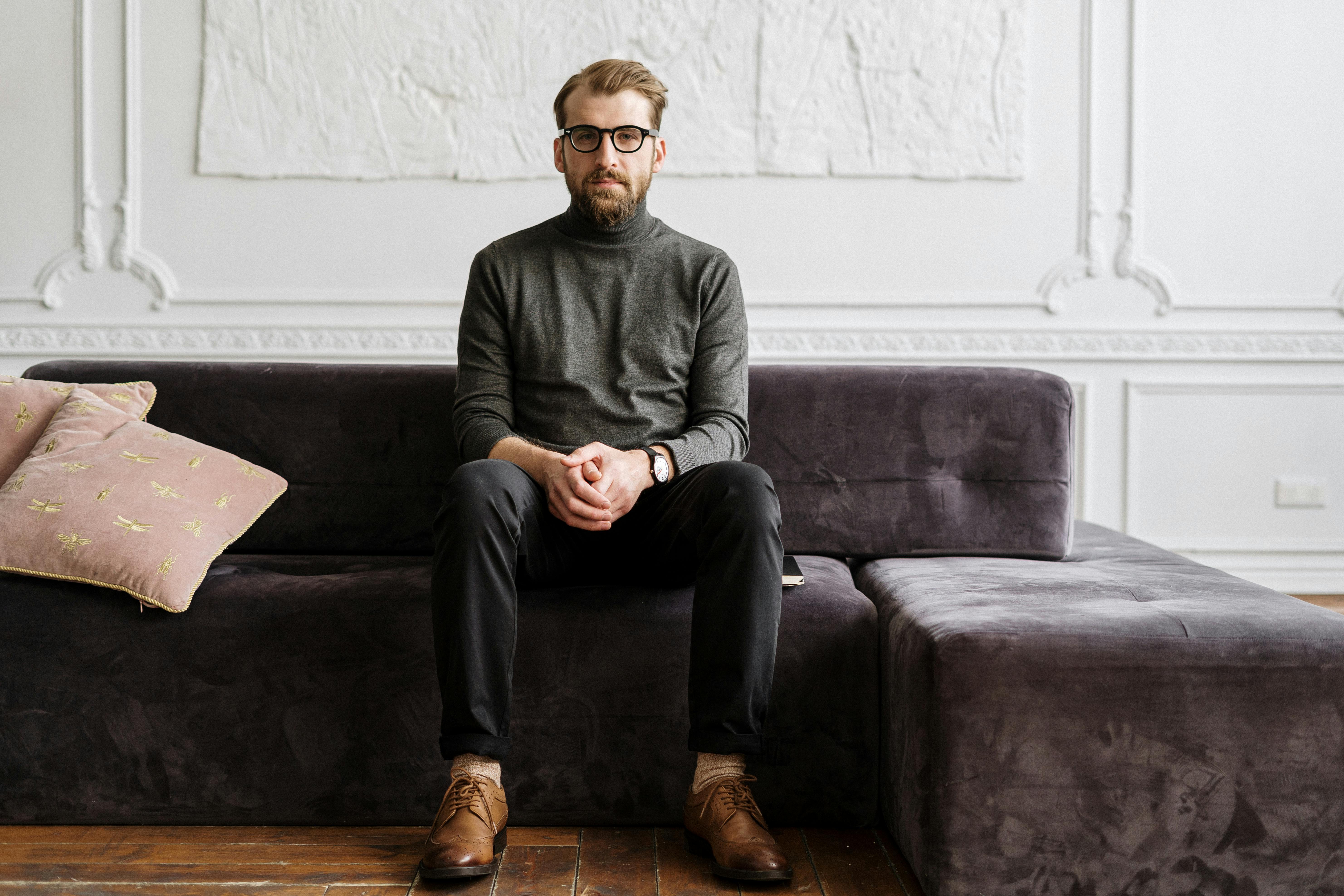 Man sitting on a gray couch in a flat, emotionless interior with dull design elements and no visual stimulation.