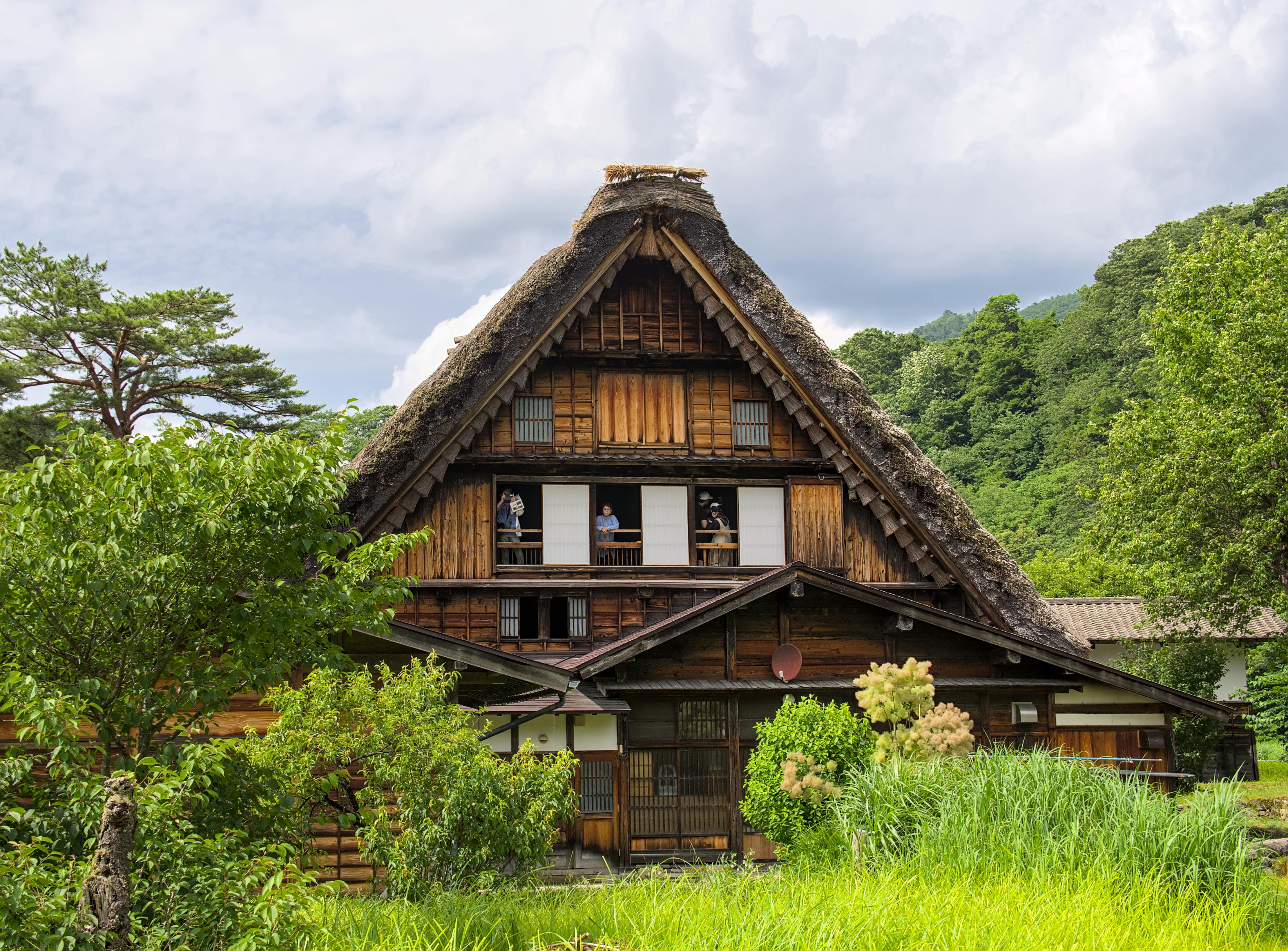 A Gassho-Zukuri house in Shirakawa-go, Japan, featuring a steep thatched roof, set in a scenic landscape.