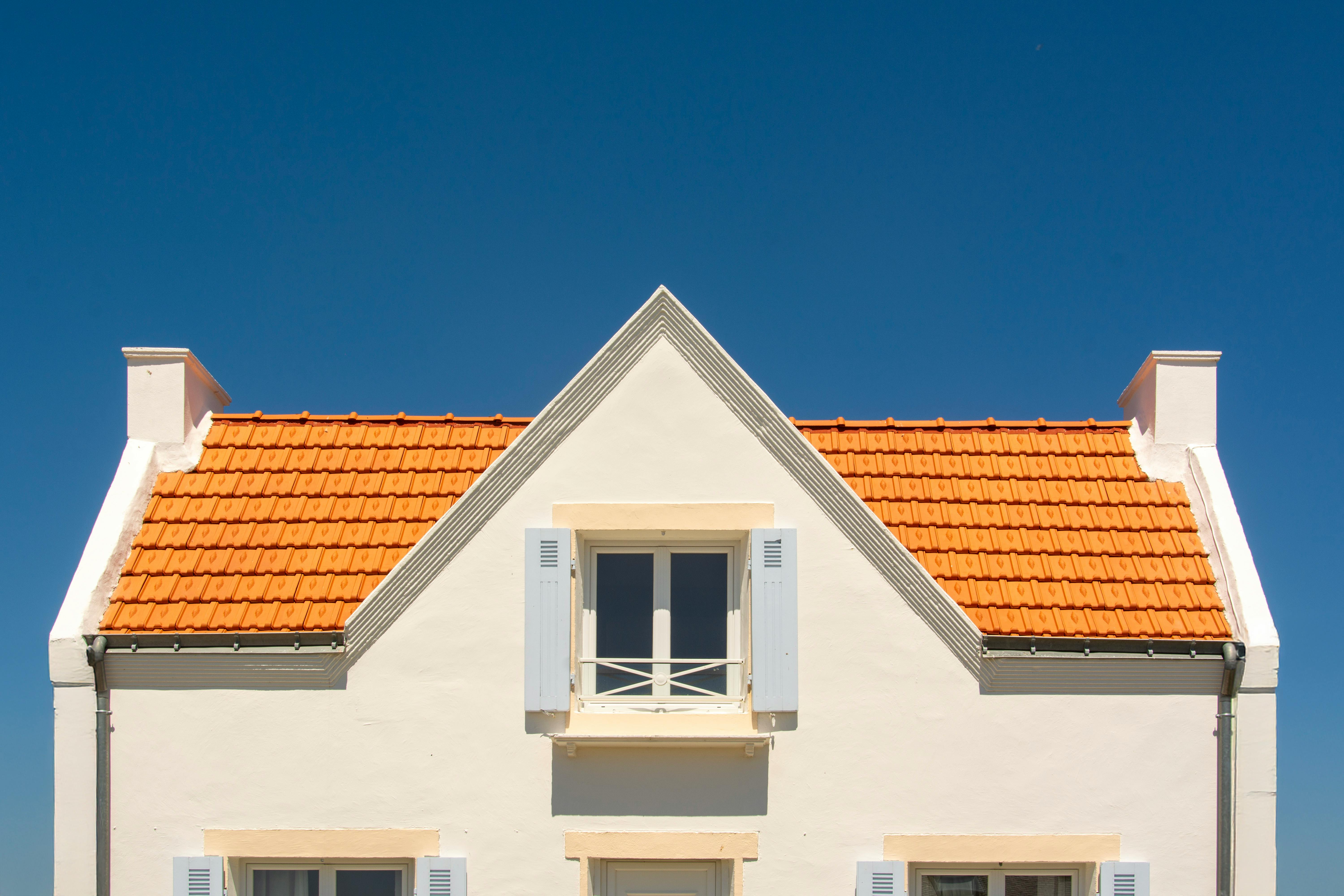 Charming house with orange tiled hip and gable roof, surrounded by greenery and clear sky.
