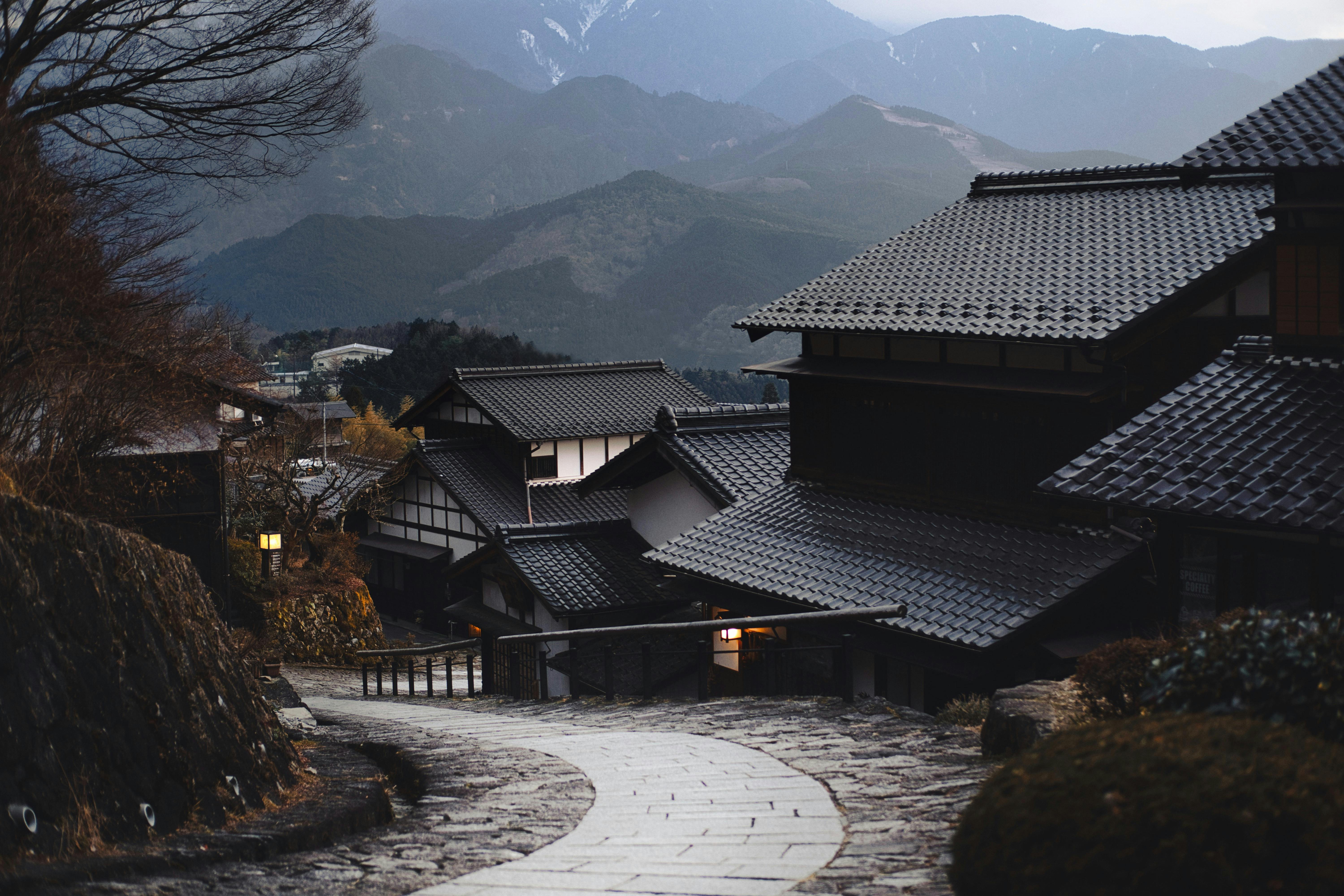 A scenic view of traditional Japanese houses with wooden exteriors, tiled roofs, and a peaceful natural setting.