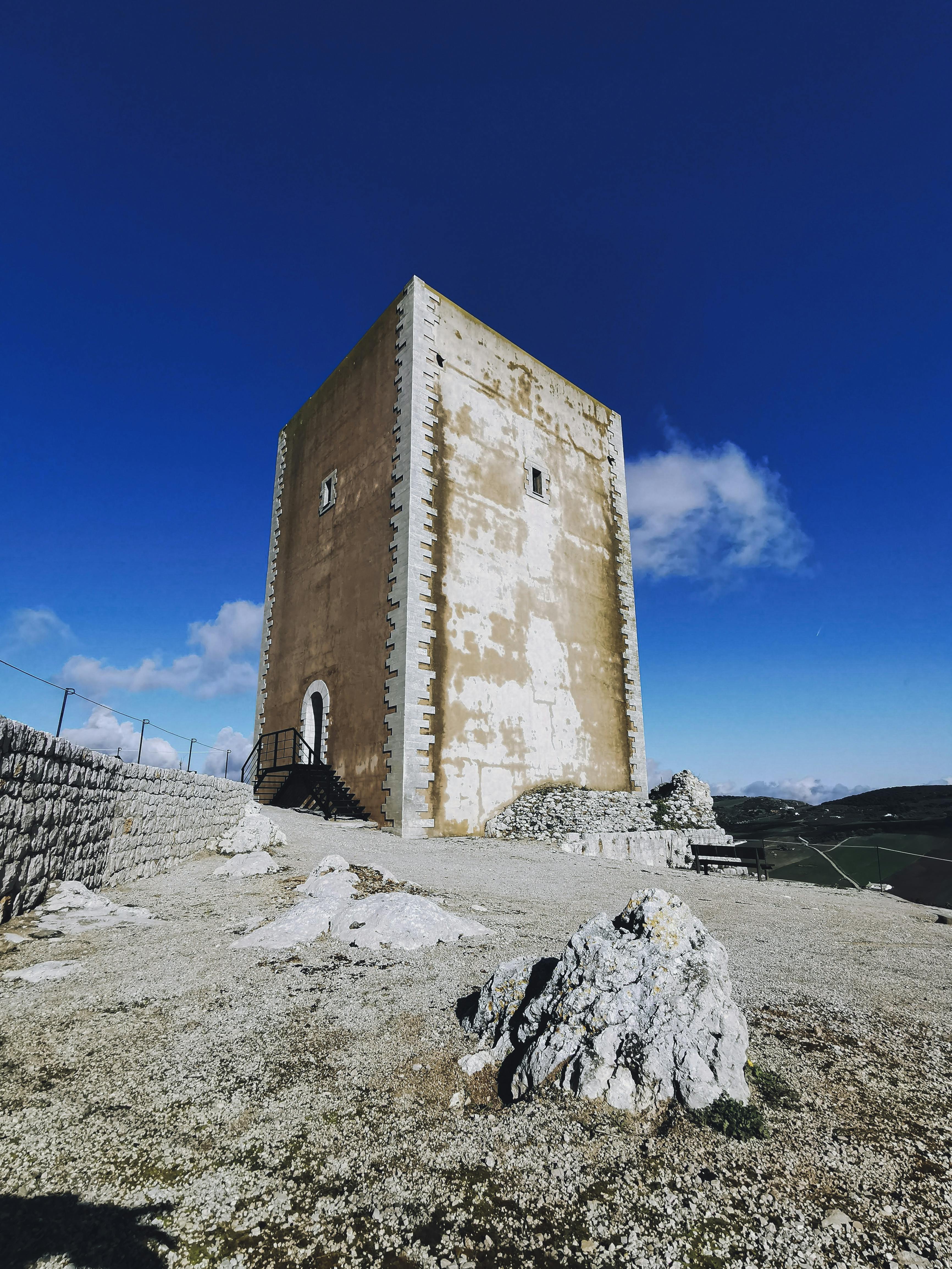 Stone medieval tower standing alone in the mountains, surrounded by rugged landscape.
