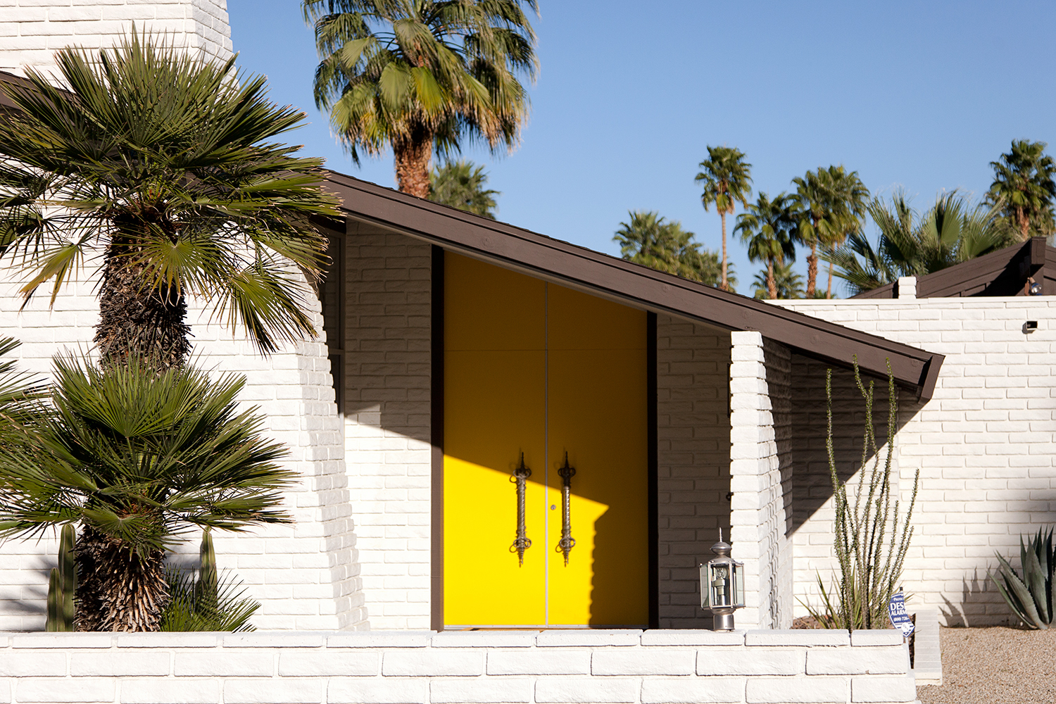 Mid-century modern house exterior in Palm Springs with clean lines, flat roof, and expansive glass windows.​