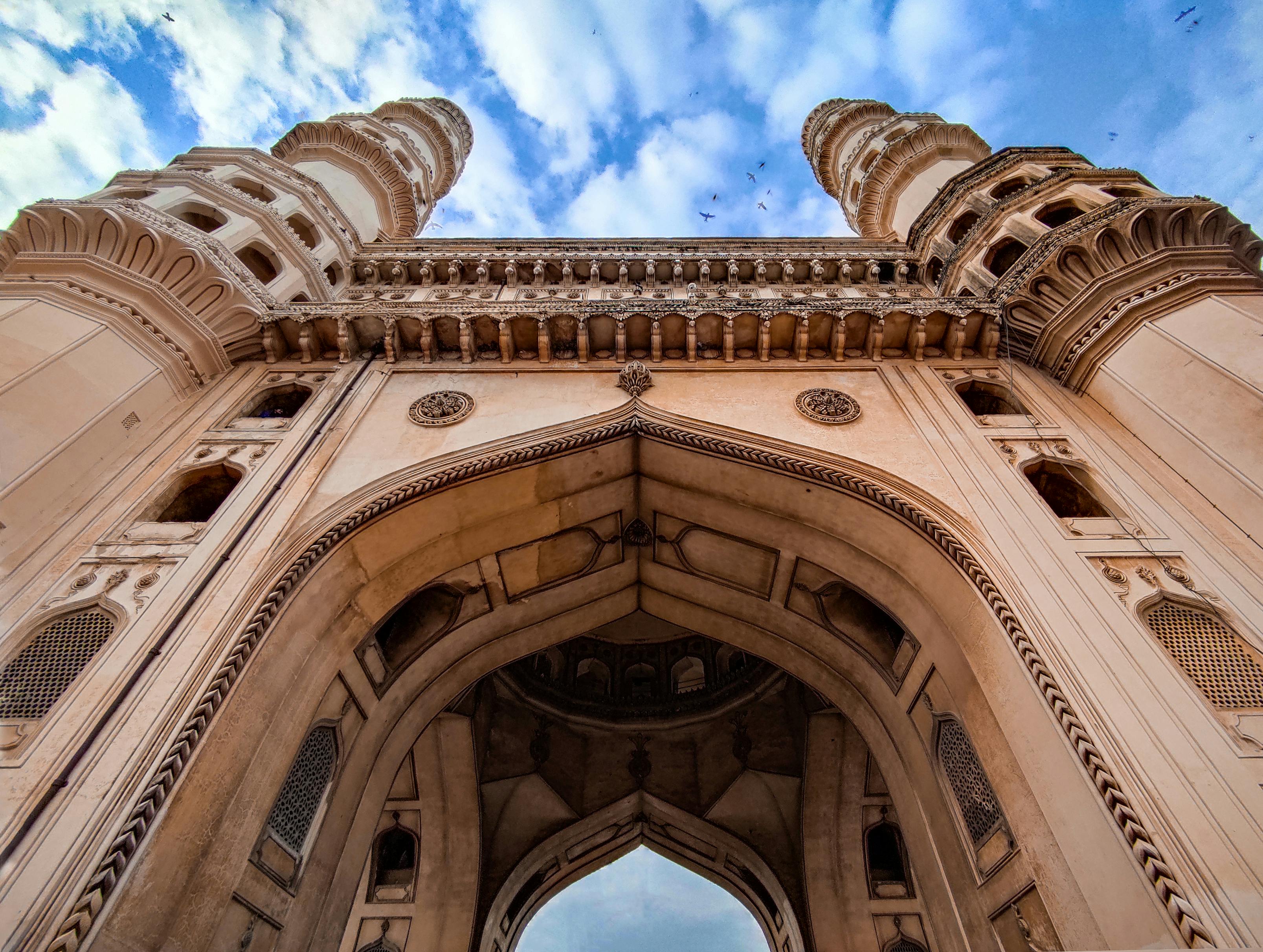 Low angle photograph of Charminar in Hyderabad, highlighting its four grand arches and symmetrical minarets in Islamic style.