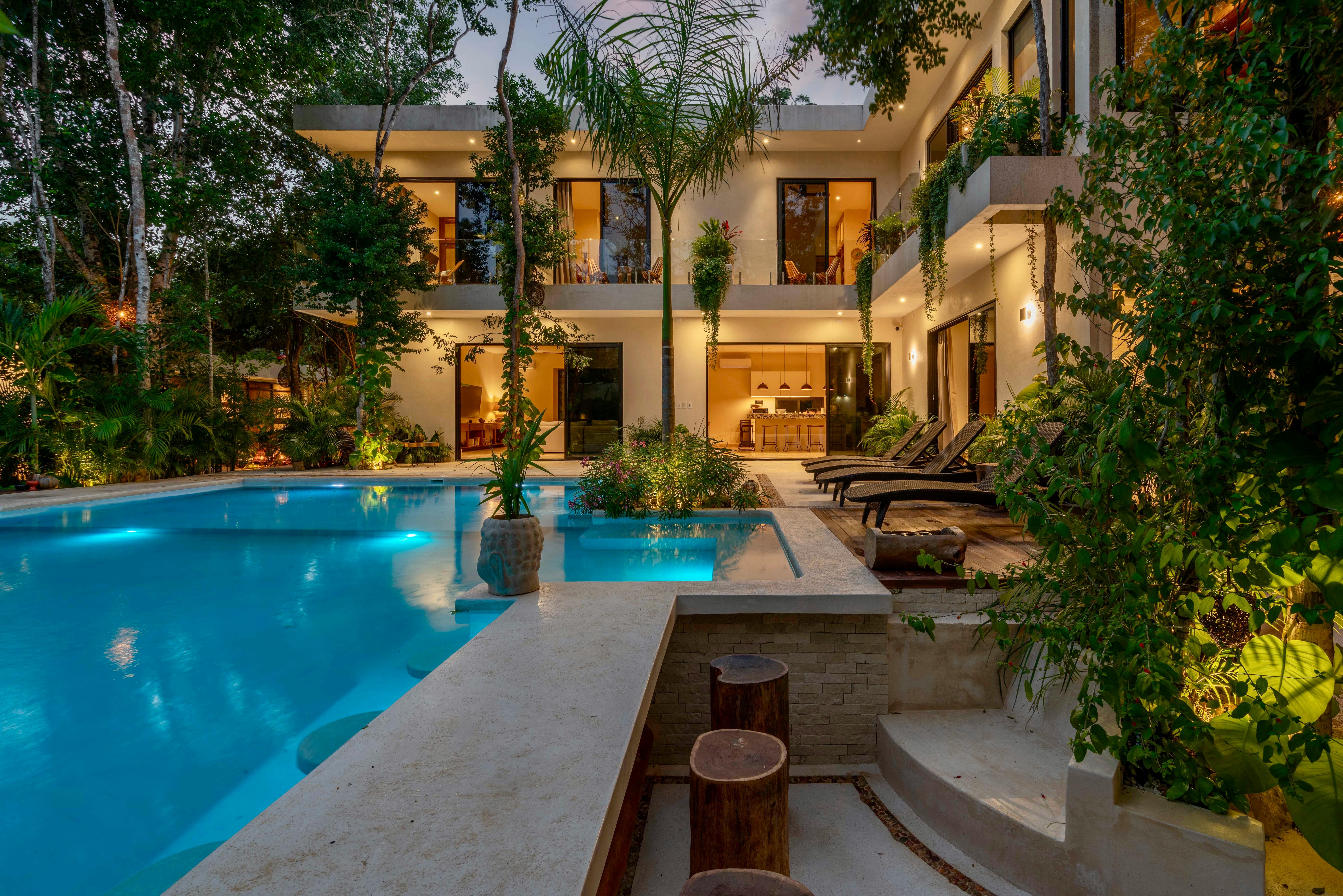 Luxury Mediterranean villa with a large swimming pool surrounded by lush plants and palm trees.