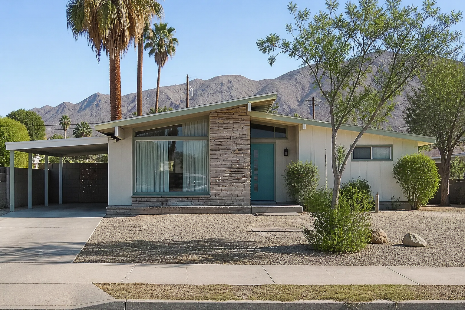 Midcentury desert ranch house with large glass, low roof, carport, and aging exterior panels.