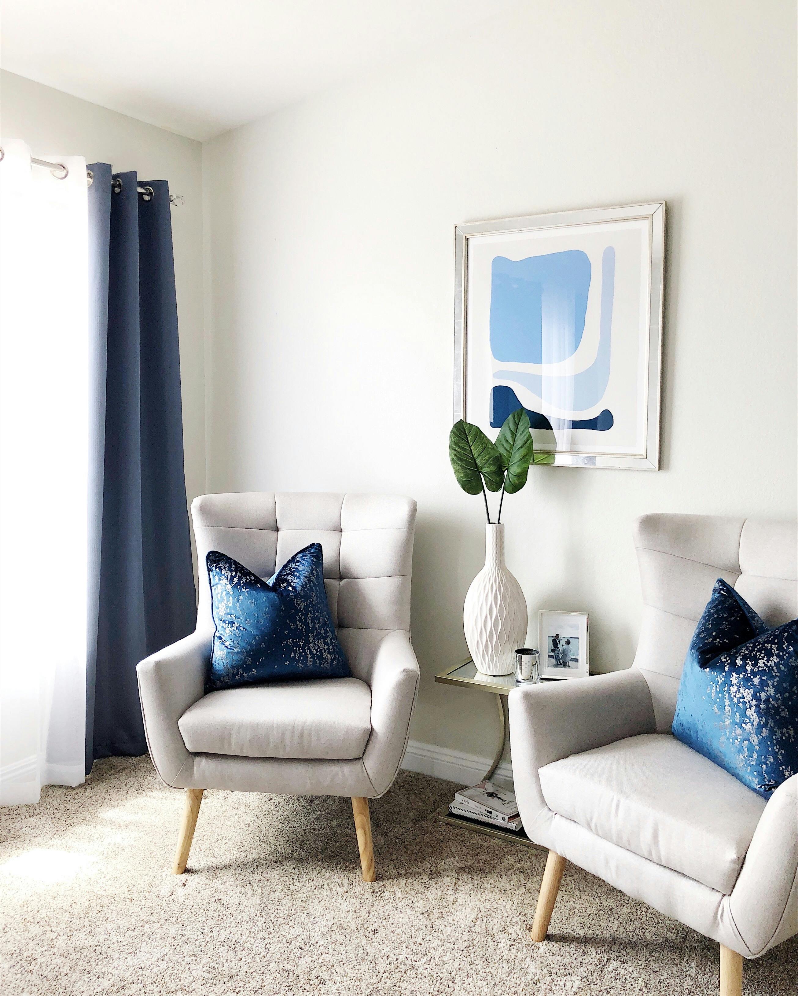Living room with light cream walls, blue curtains, and colorful cushions.