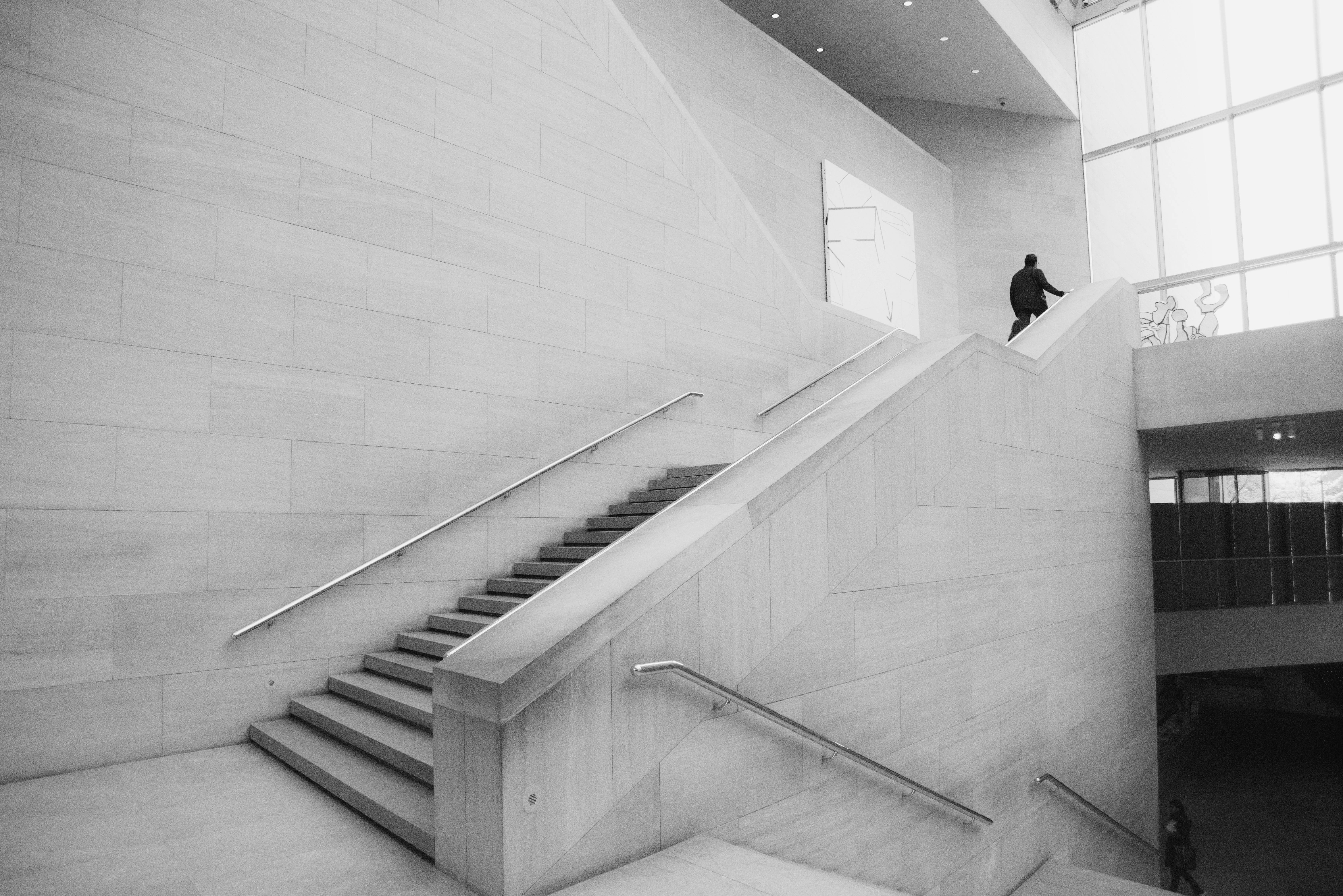 Person ascending wide museum stairs in vast interior.