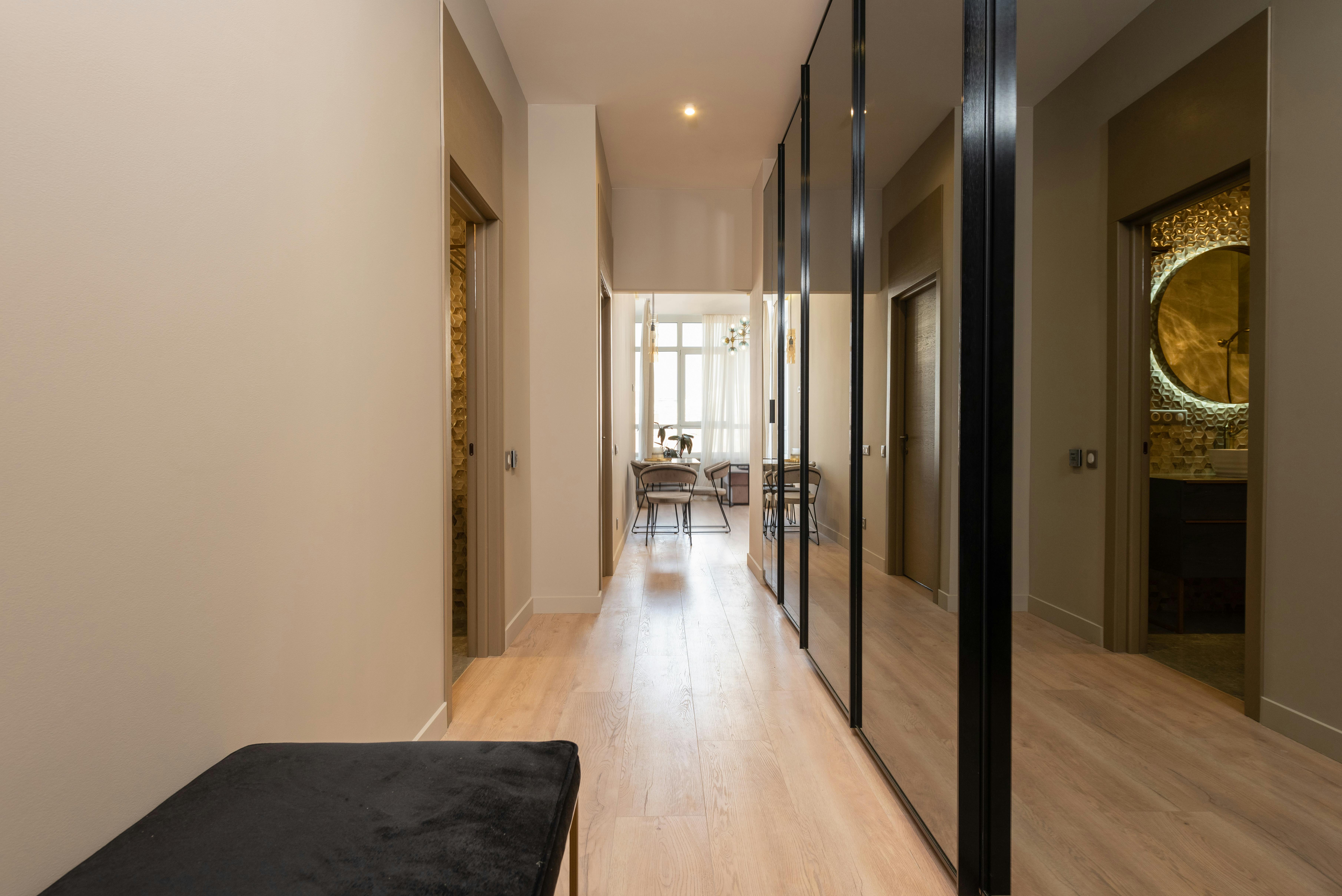 Modern apartment corridor with mirrors near the doorway and warm neutral tones.