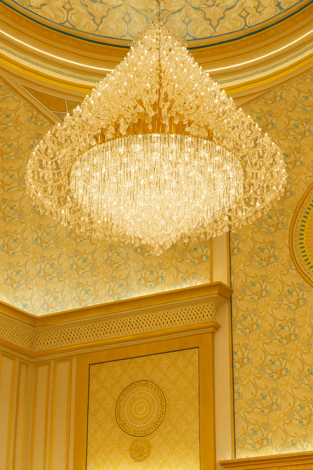 Crystal Art Deco chandelier with gold frame hanging from ornate golden ceiling.