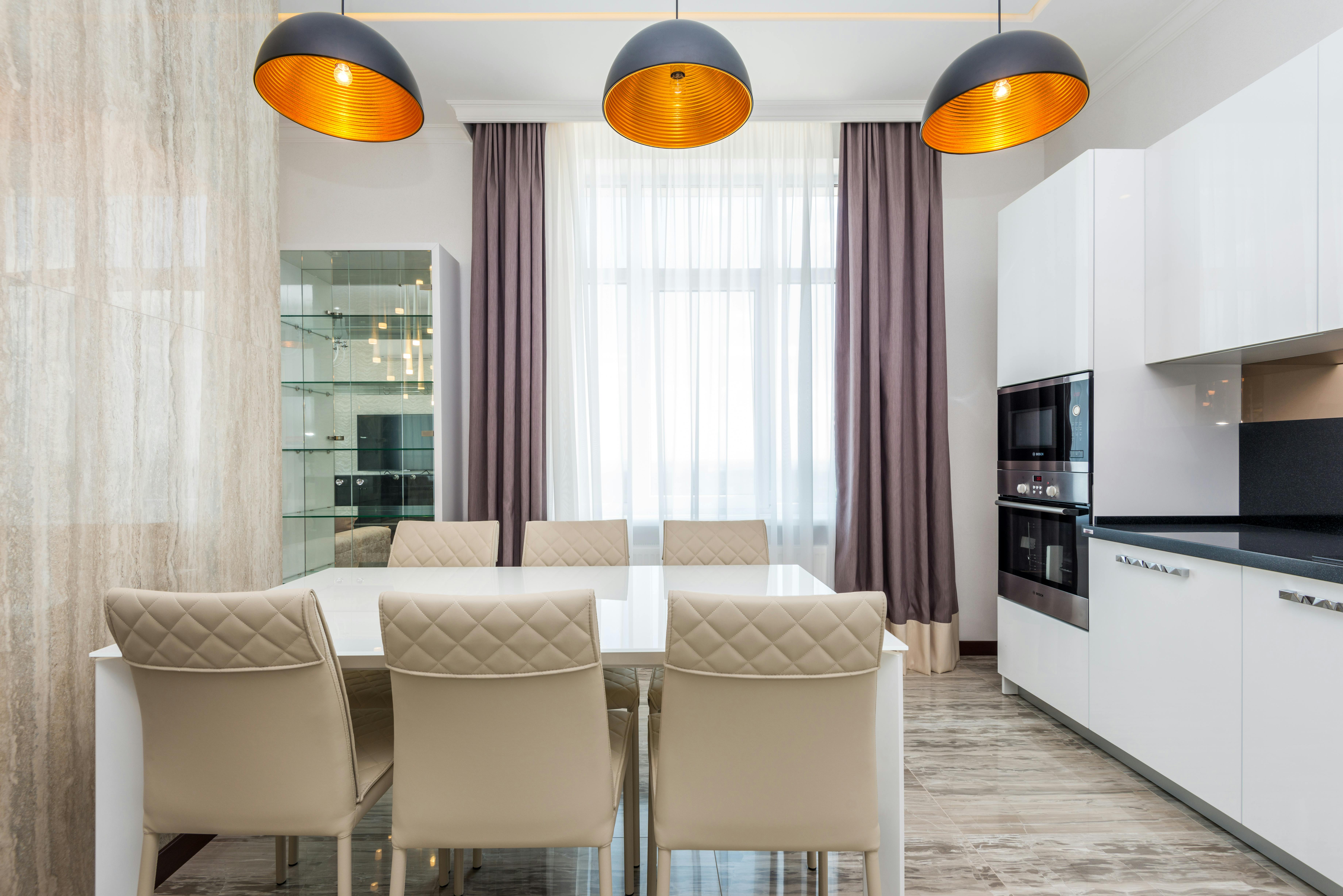 Dining table and beige chairs in modern kitchen with pendant lights.