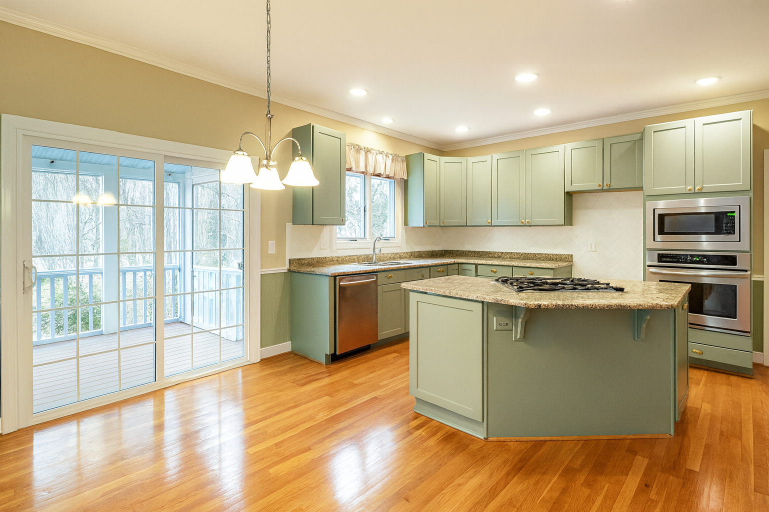 Kitchen with muted sage green cabinets, brass hardware, stone countertops, and natural wood floors.