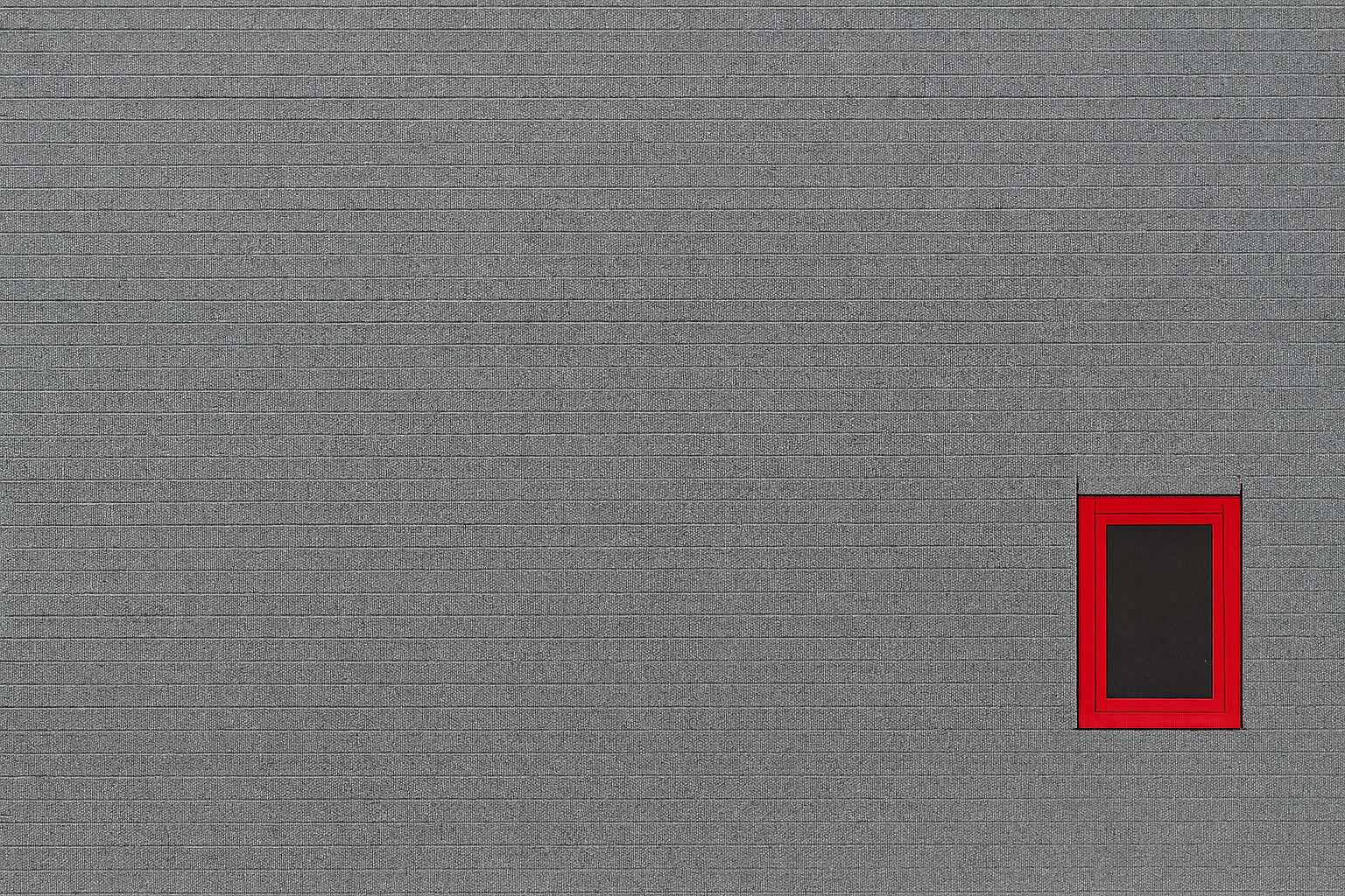 Minimalist gray wall with a single modern window framed in bold red showing color contrast in architecture.