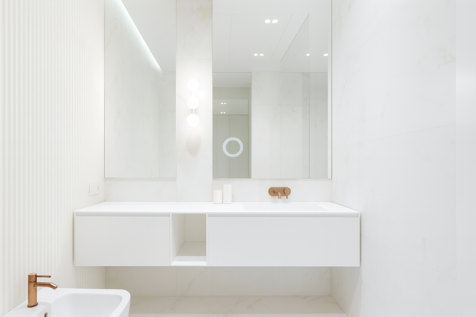 Modern all-white bathroom interior with marble walls, floating vanity, and soft diffused vanity lighting.