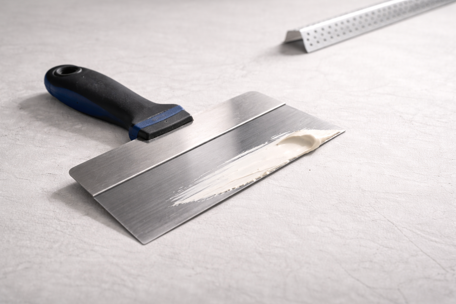 Drywall taping knife with joint compound on blade, used for mudding and finishing seams.