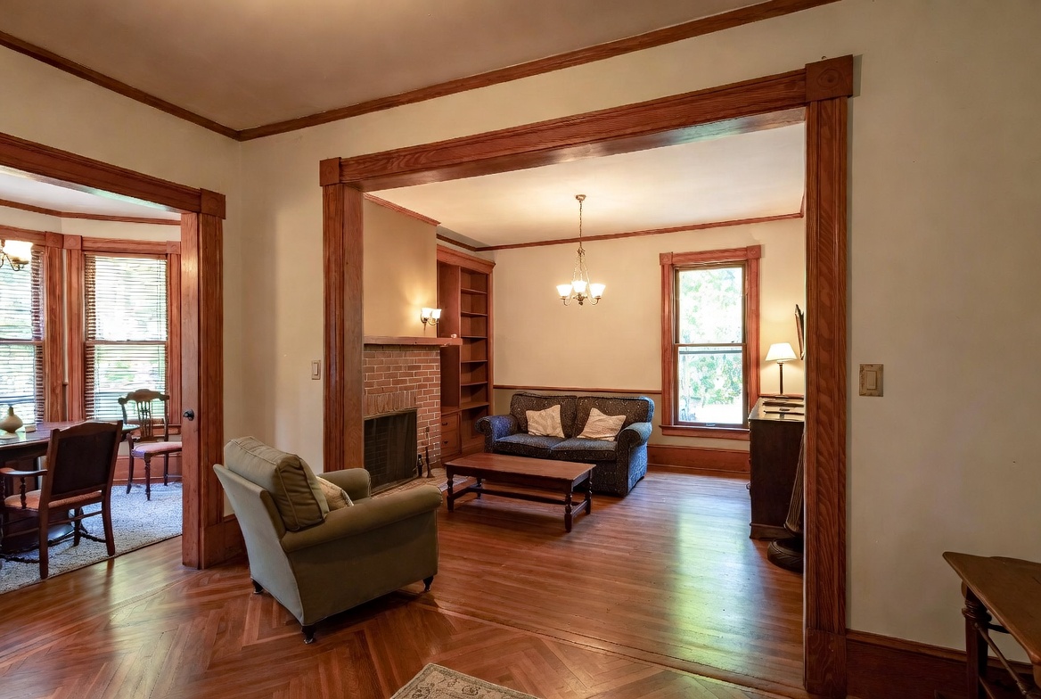 1920s interior showing wood trim, wide room opening, fireplace, and defined living-room layout.