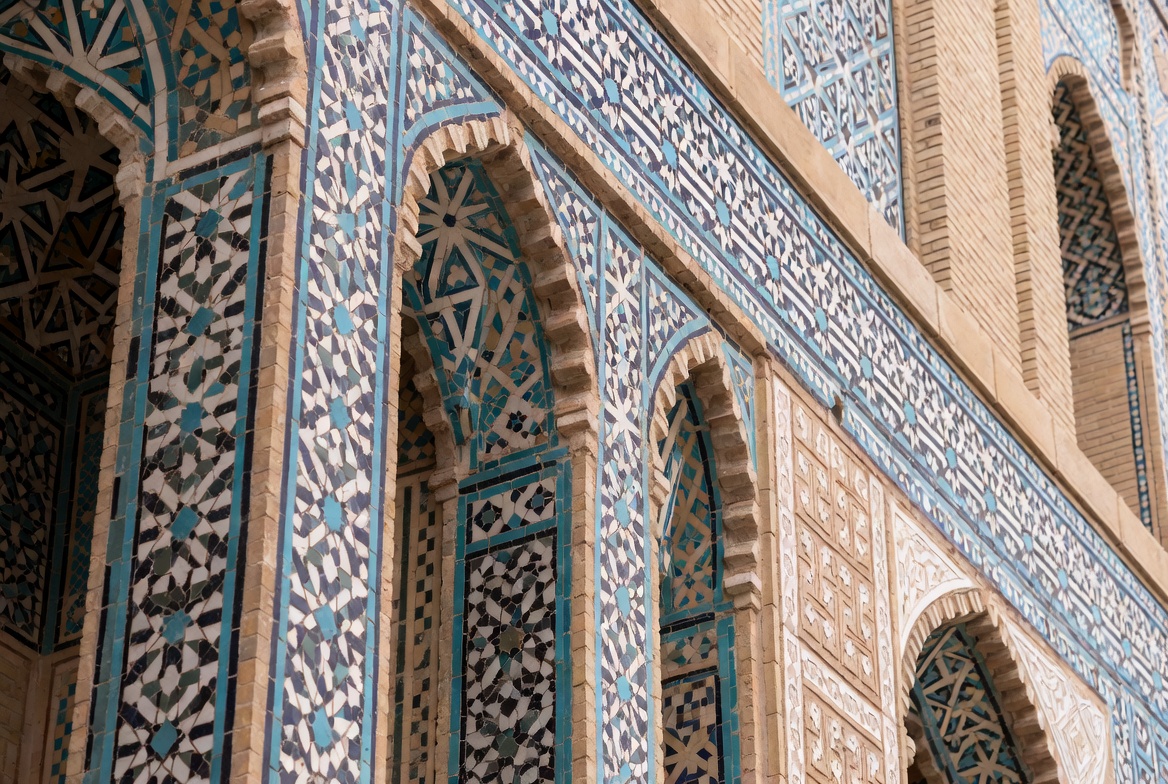 Arabic geometric tilework on arched facade with blue mosaic patterns and carved architectural detail.