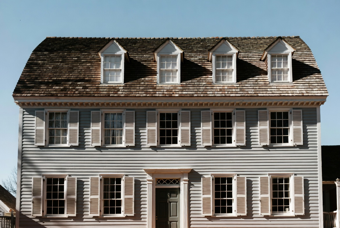 Colonial house with symmetrical facade, centered entrance, black shutters, and twin chimneys.