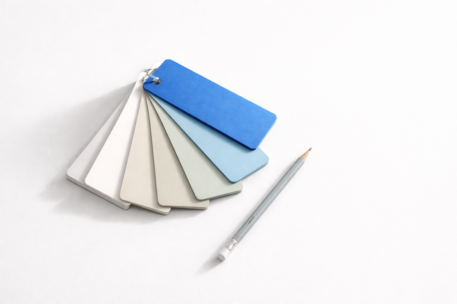 Paint swatch fan with one cobalt blue card beside a pencil on a white surface.