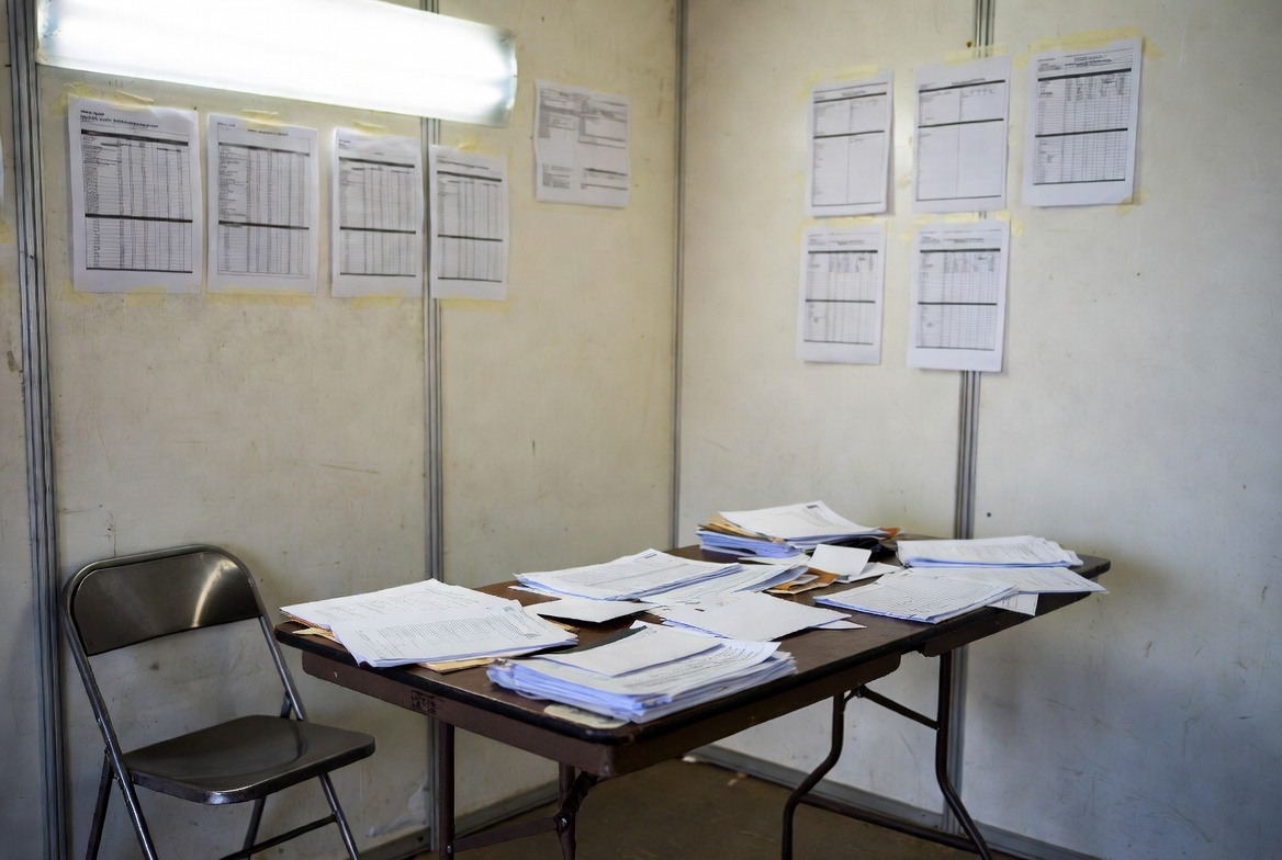 Bid review papers on a table and a wall inside a temporary site office during the construction tender and evaluation process.