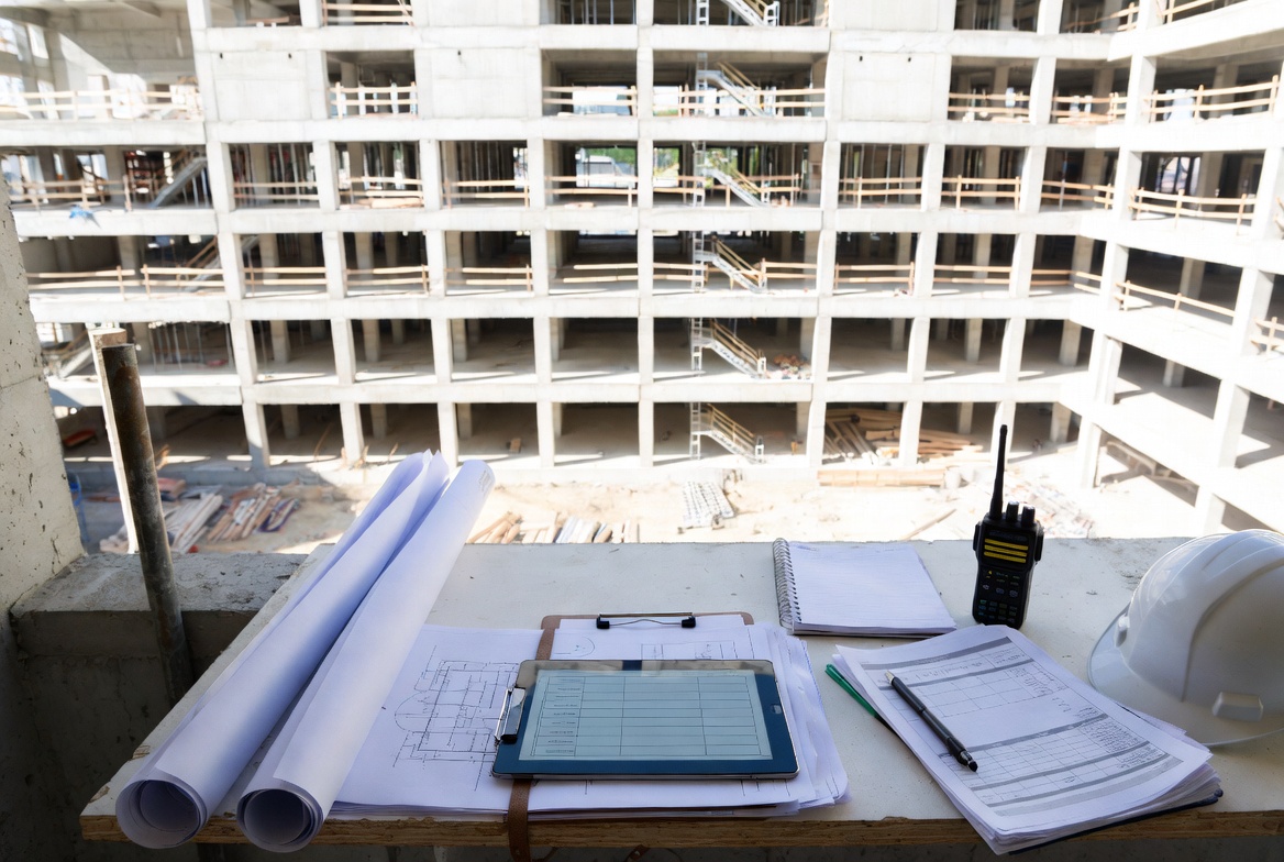 Construction project management setup with plans and tablet overlooking an active building site.
