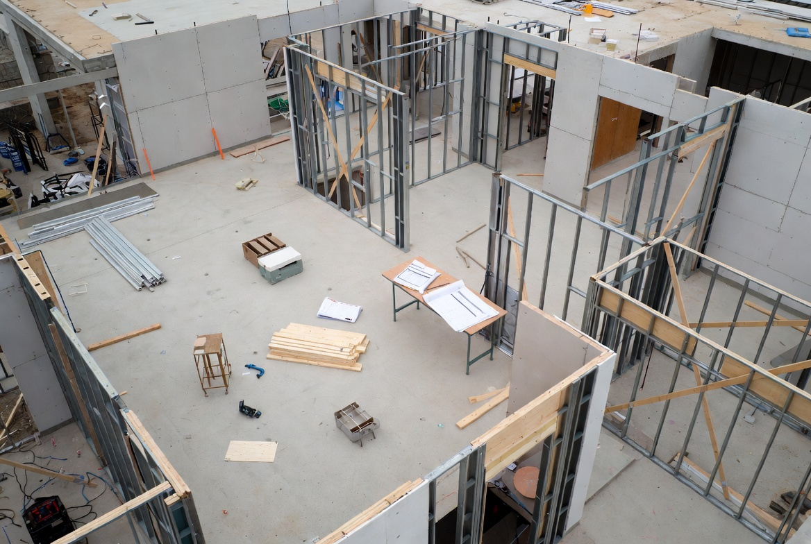 Top-down view of an under-construction building showing metal stud framing and construction materials laid out on the concrete floor.