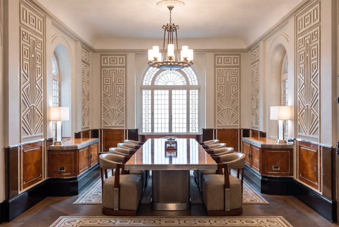 Formal Art Deco dining room with geometric wall framing, polished wood furniture, and symmetrical lighting.
