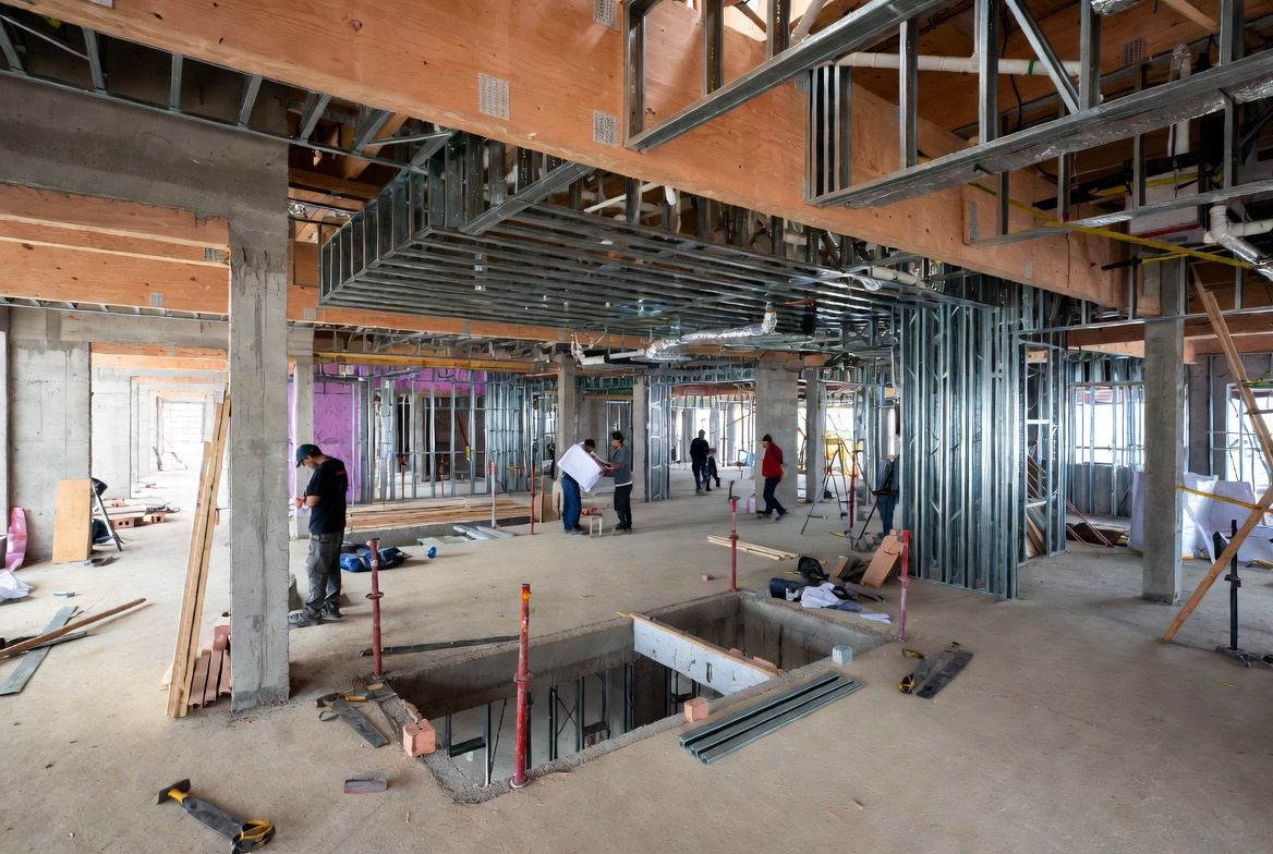 Ground-level framing and ductwork in a healthcare construction site with exposed studs and concrete columns.