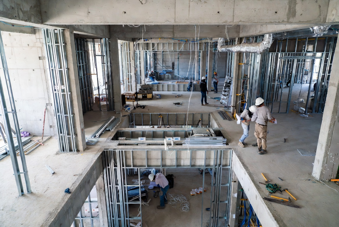 Interior of healthcare construction site showing mechanical ducts, steel stud walls, and early ceiling framing.