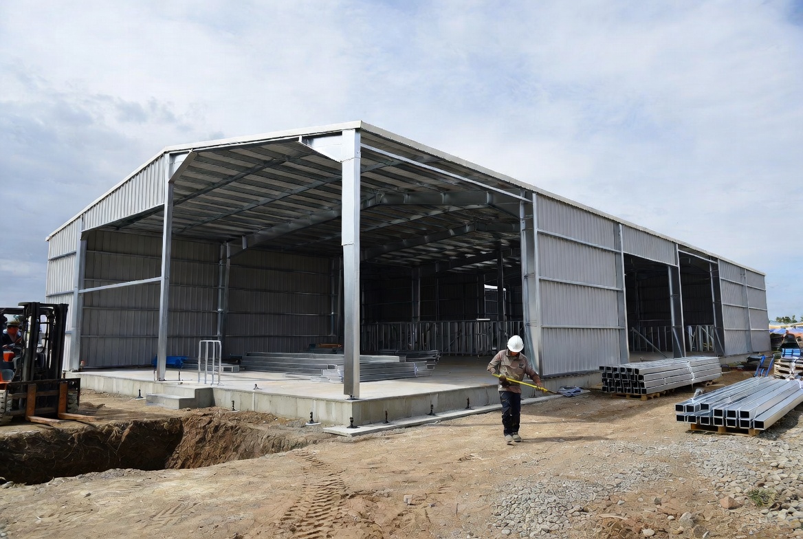 Prefab metal building erection on a concrete slab with workers, steel framing, and active site work.