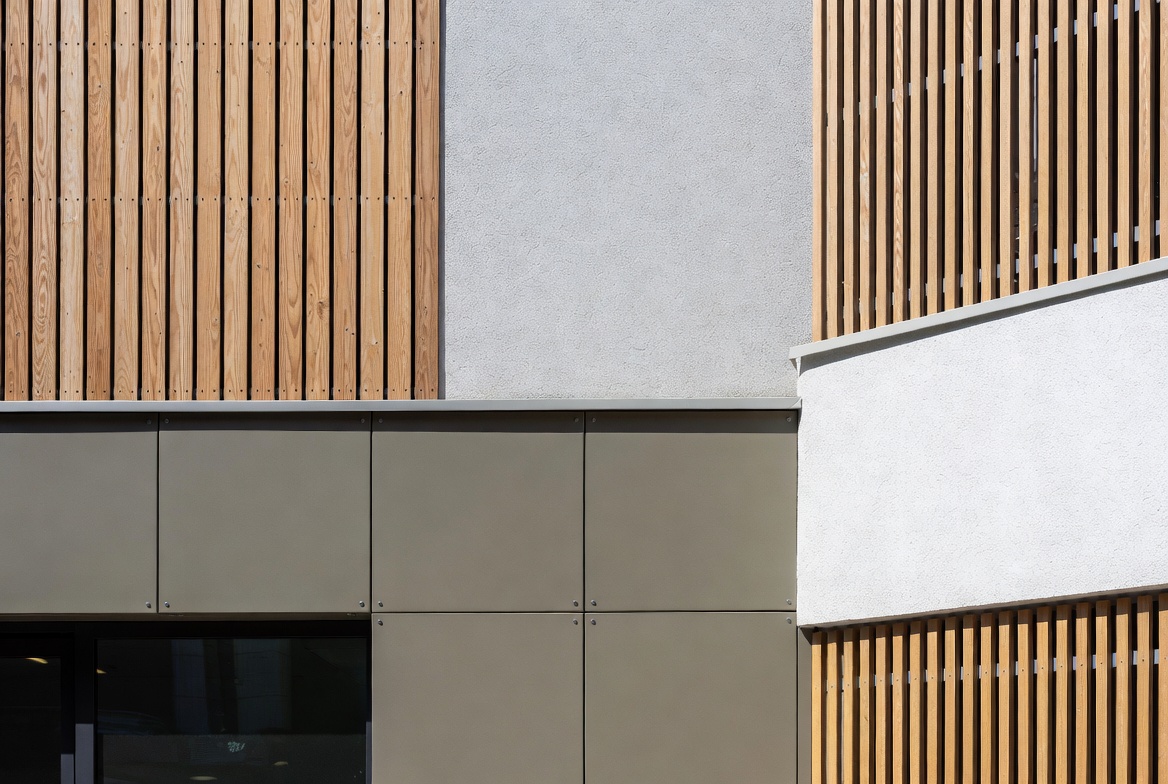Modern facade combining vertical timber slats, light render, and panelized cladding at a building corner.