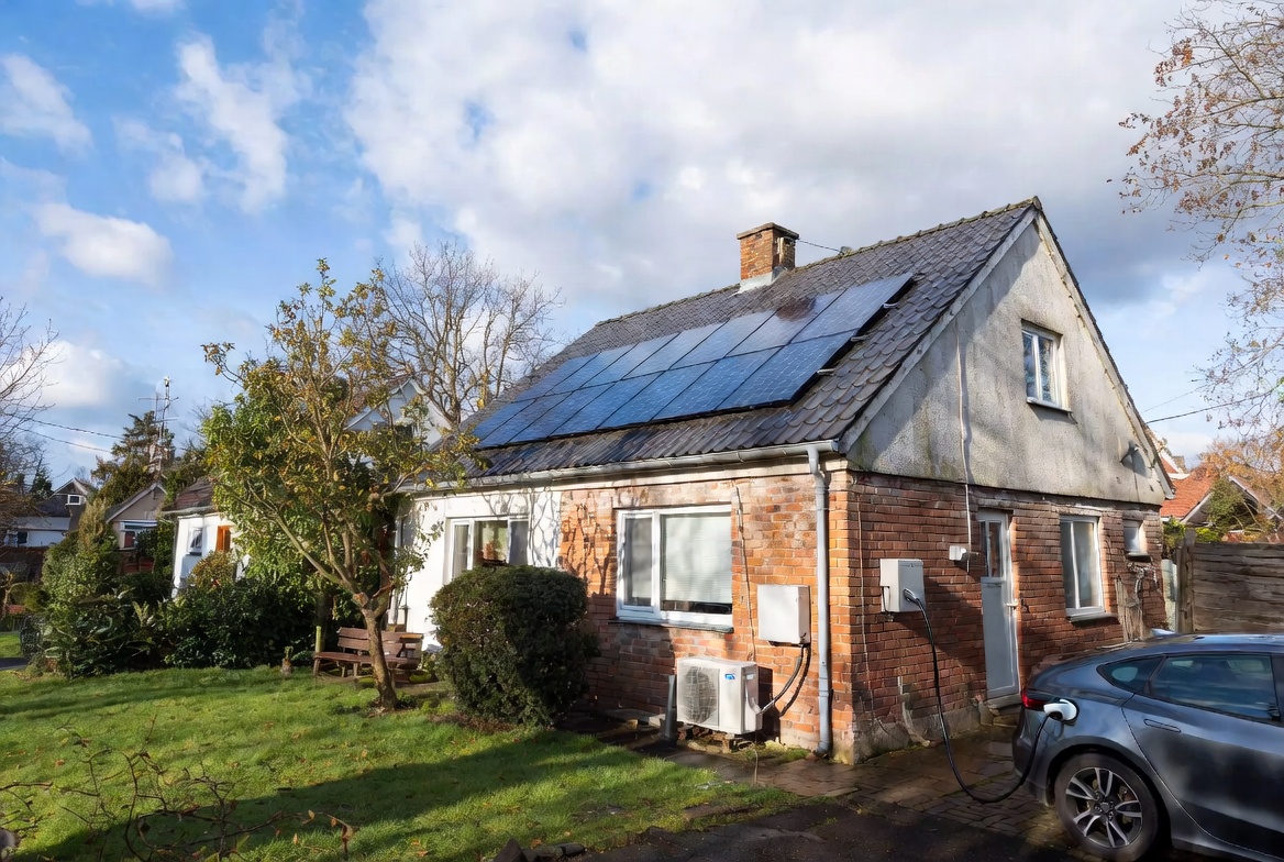 Older house with rooftop solar panels, heat pump, and parked electric car.